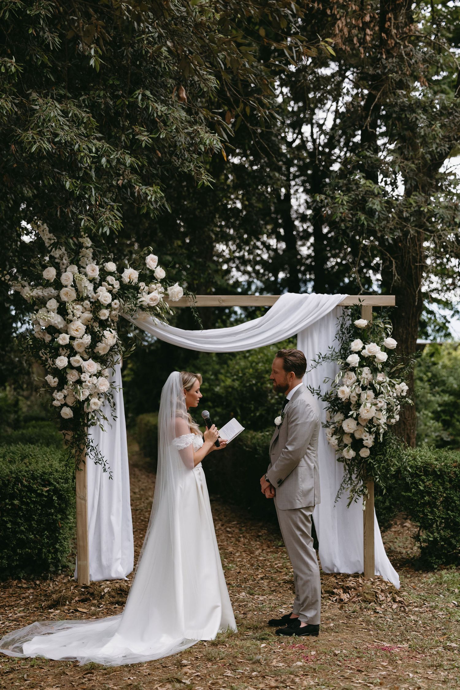 Outdoor wedding ceremony setup with white drapery arch and floral arrangements.