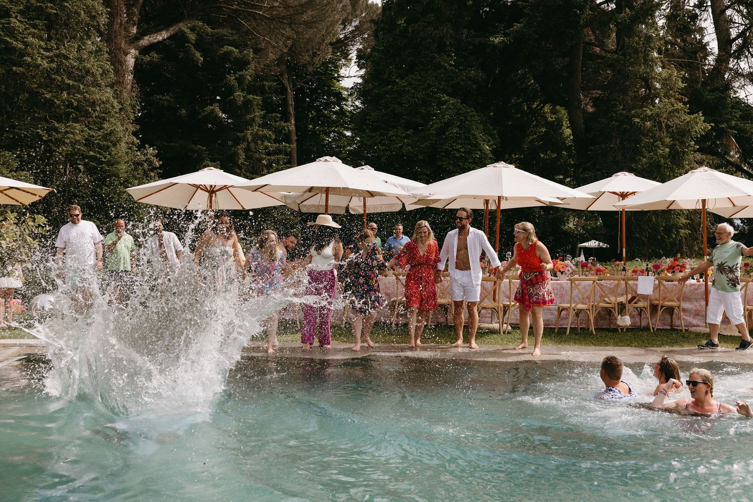People creating splashes in a swimming pool during a festive outdoor event.