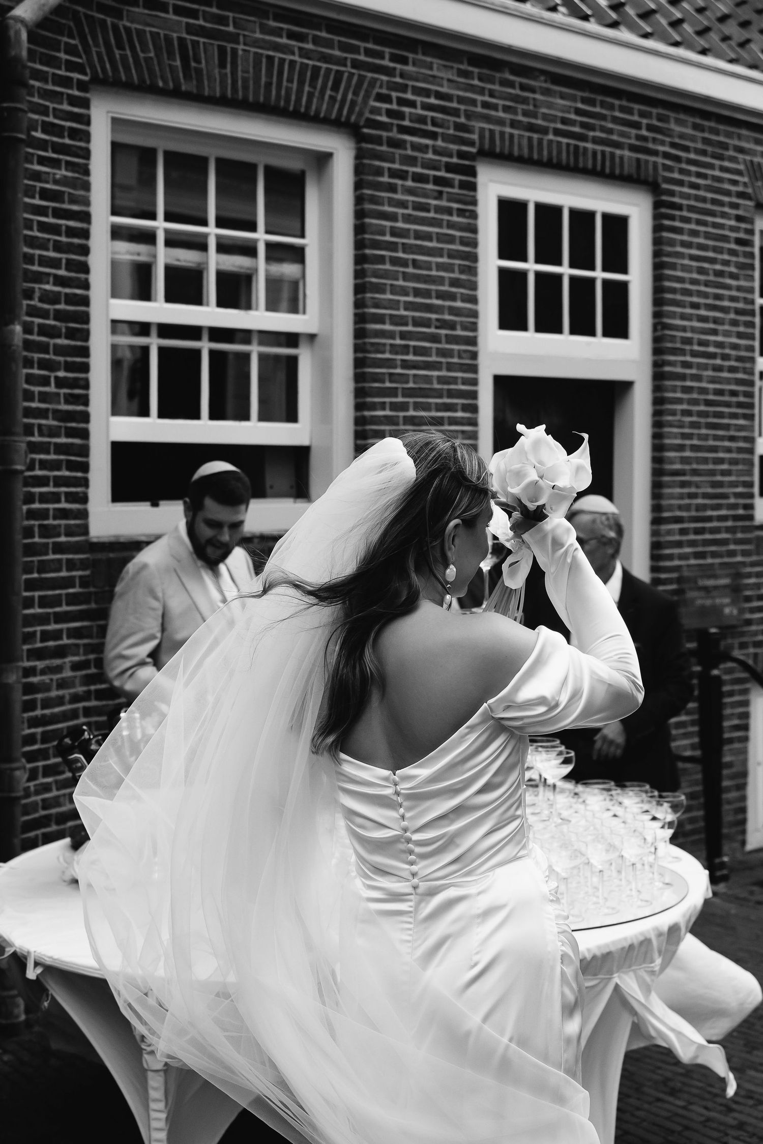 White wedding dresses flowing in motion against a brick building backdrop.