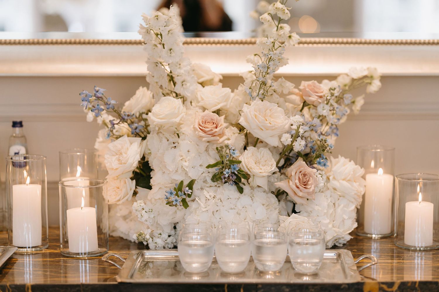 Romantic wedding decor featuring white floral arrangement with roses and candles on mirrored surface.