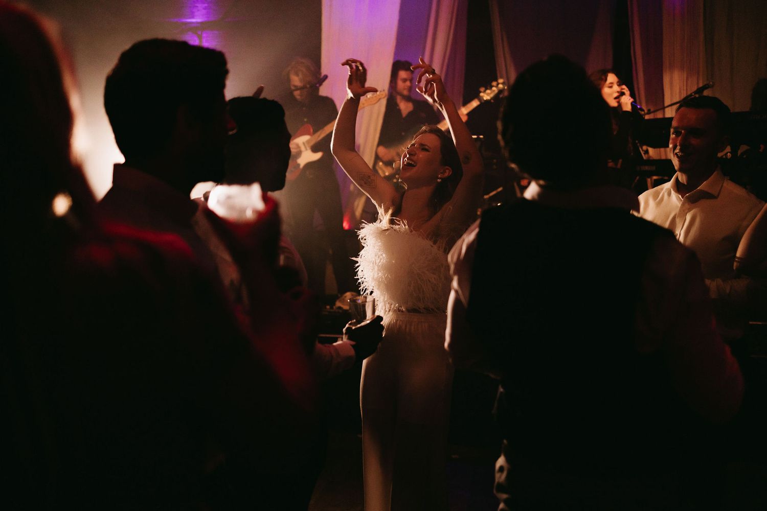 Silhouettes of wedding guests dancing in a dimly lit reception venue.