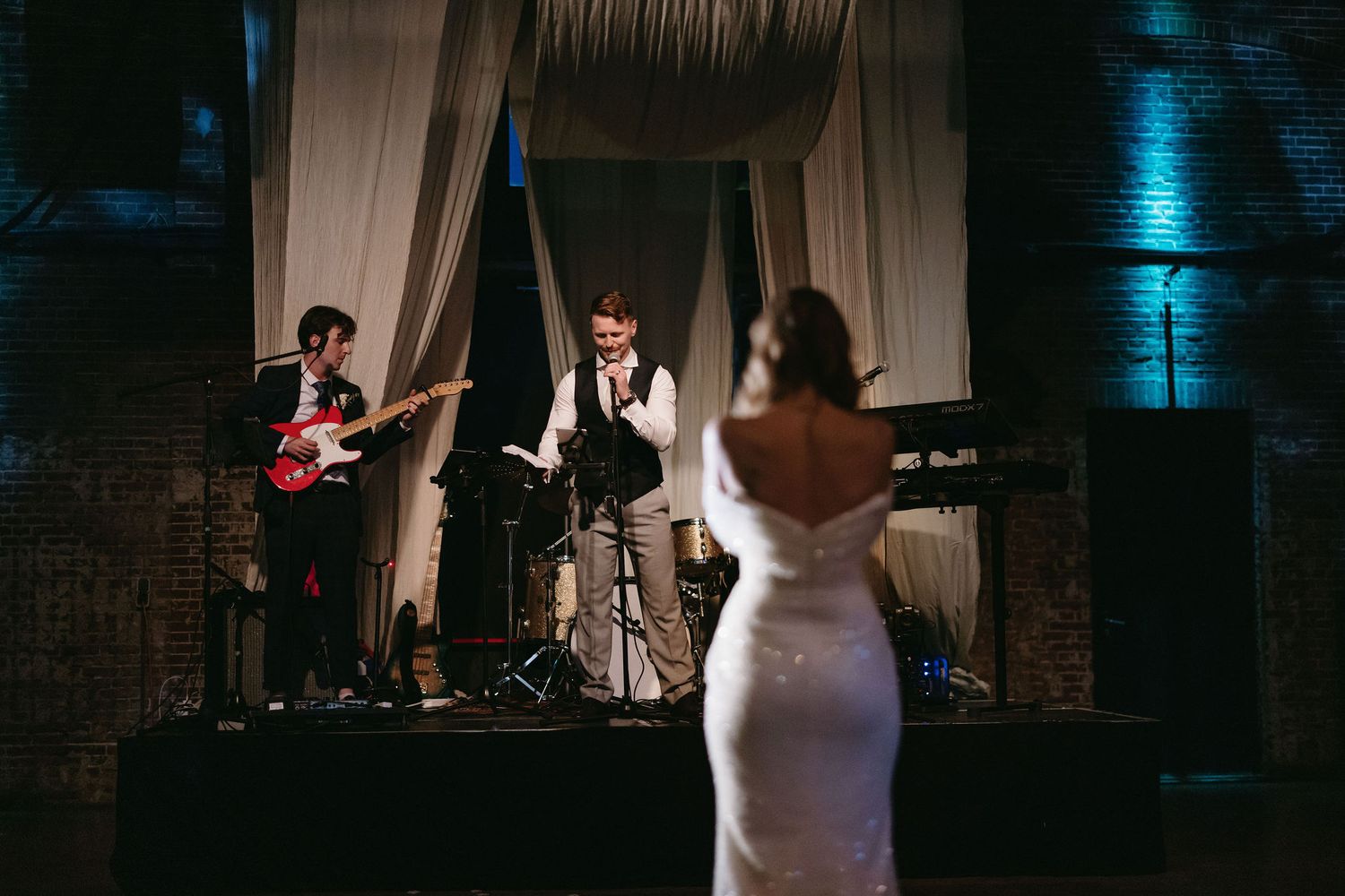 Wedding reception dance floor scene with dramatic blue lighting and white drapes.