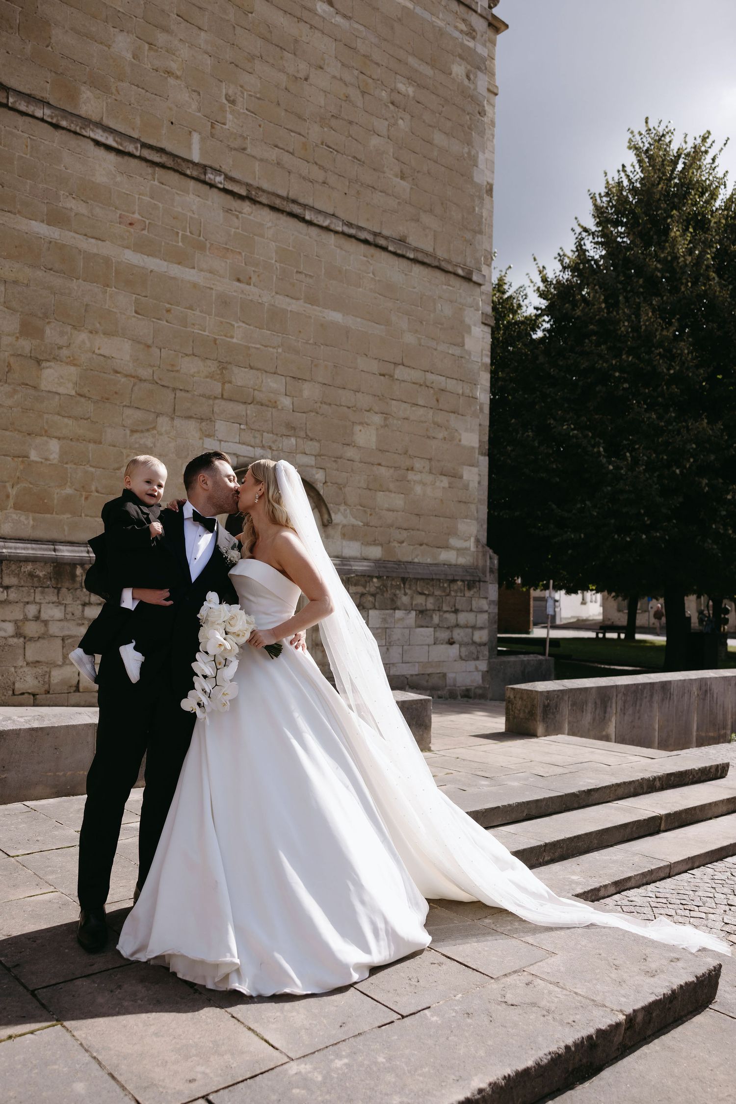 Newlyweds share romantic moment on stone steps outside historic building.