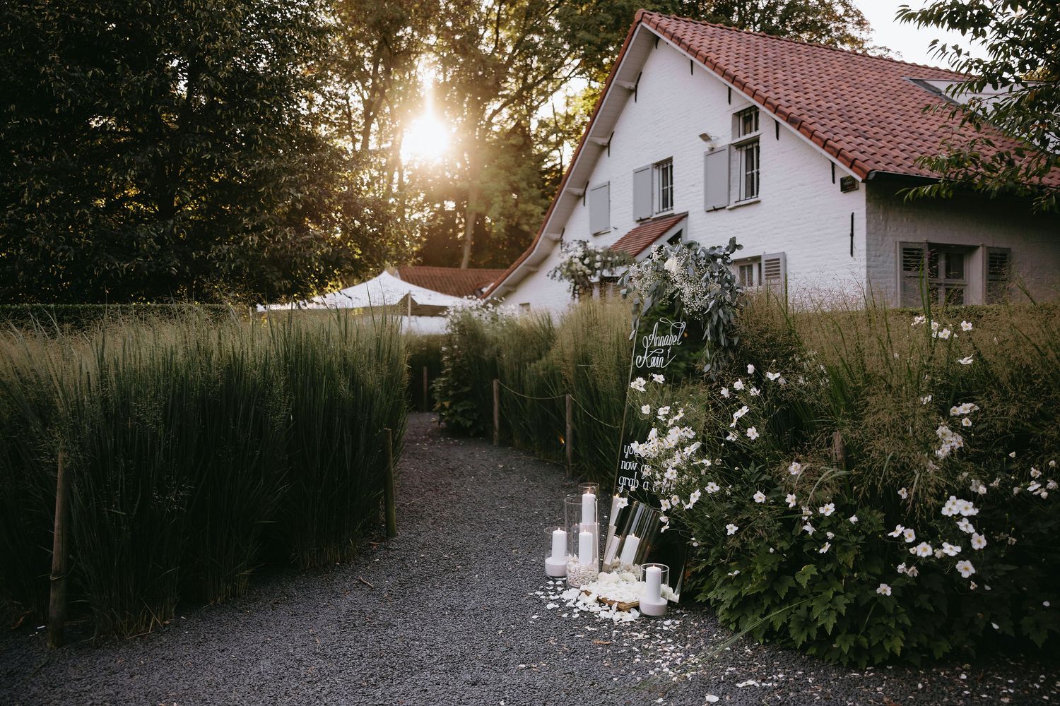 Sunset view of white country house with gravel path and garden flowers.