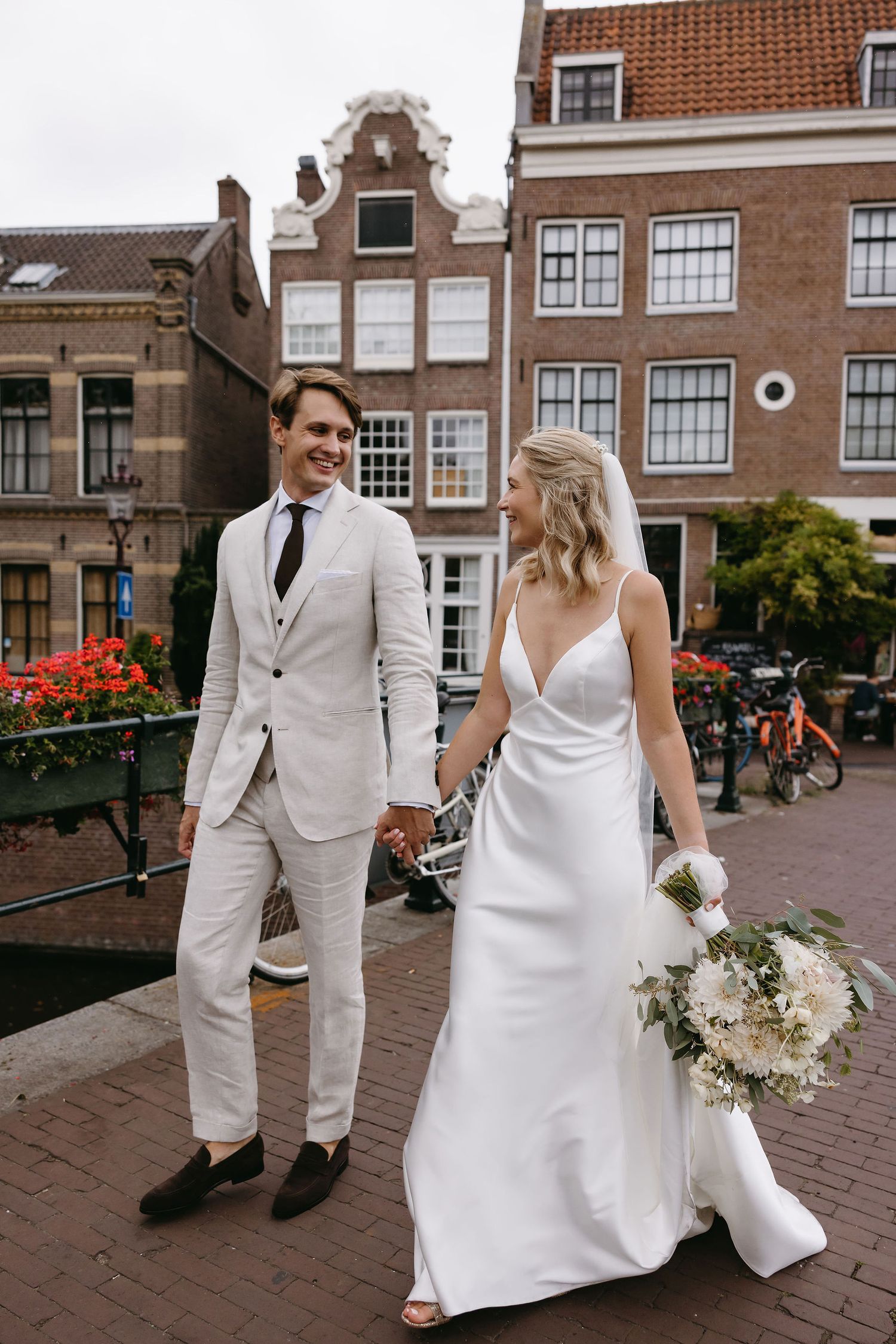 A bride and groom pose on a cobblestone street in Amsterdam with traditional Dutch architecture in the background.