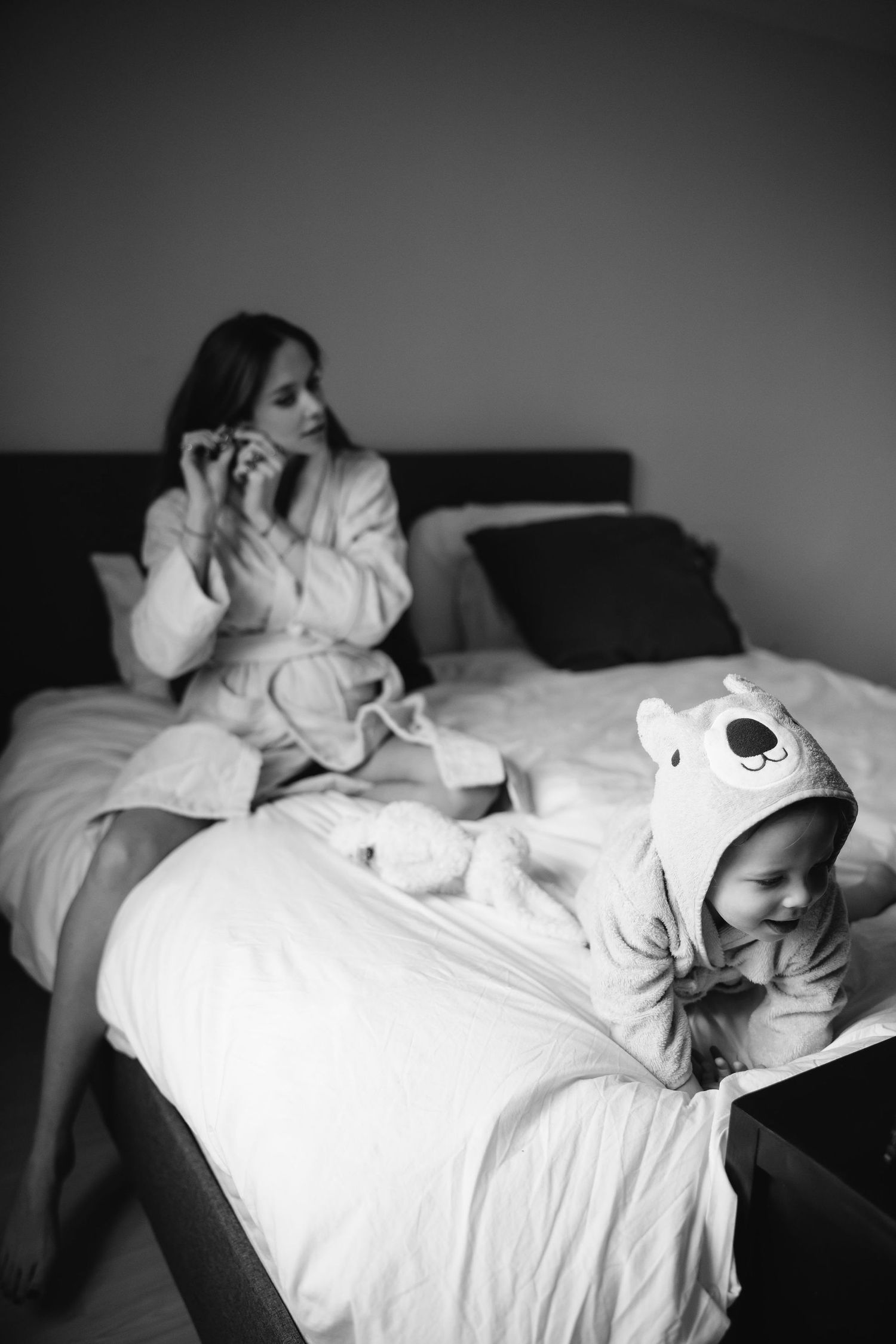 A cozy bedroom scene showing a small child in a bear hood reclining on white bedding.