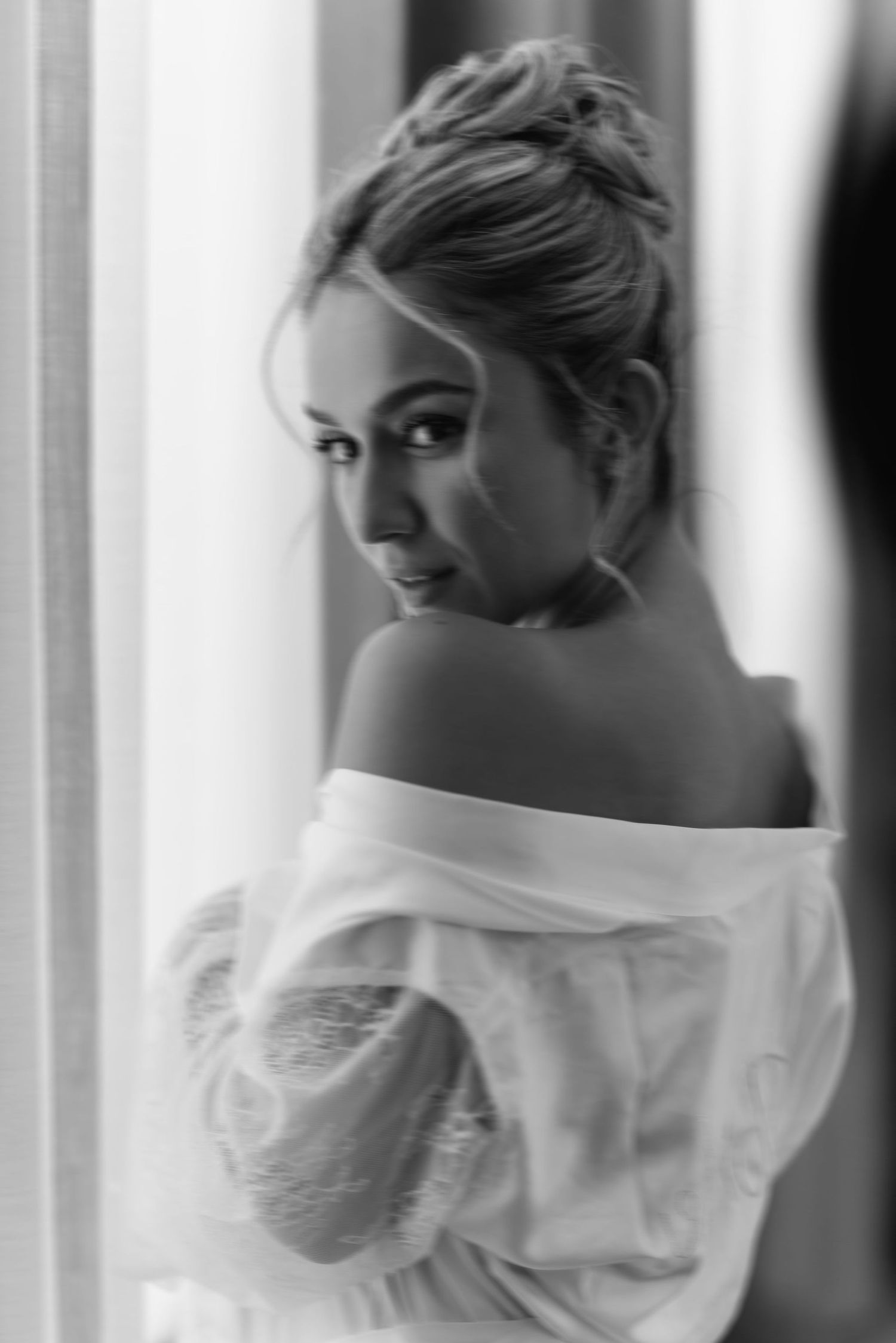 A romantic black and white portrait shows an elegant off-shoulder pose in soft window light.