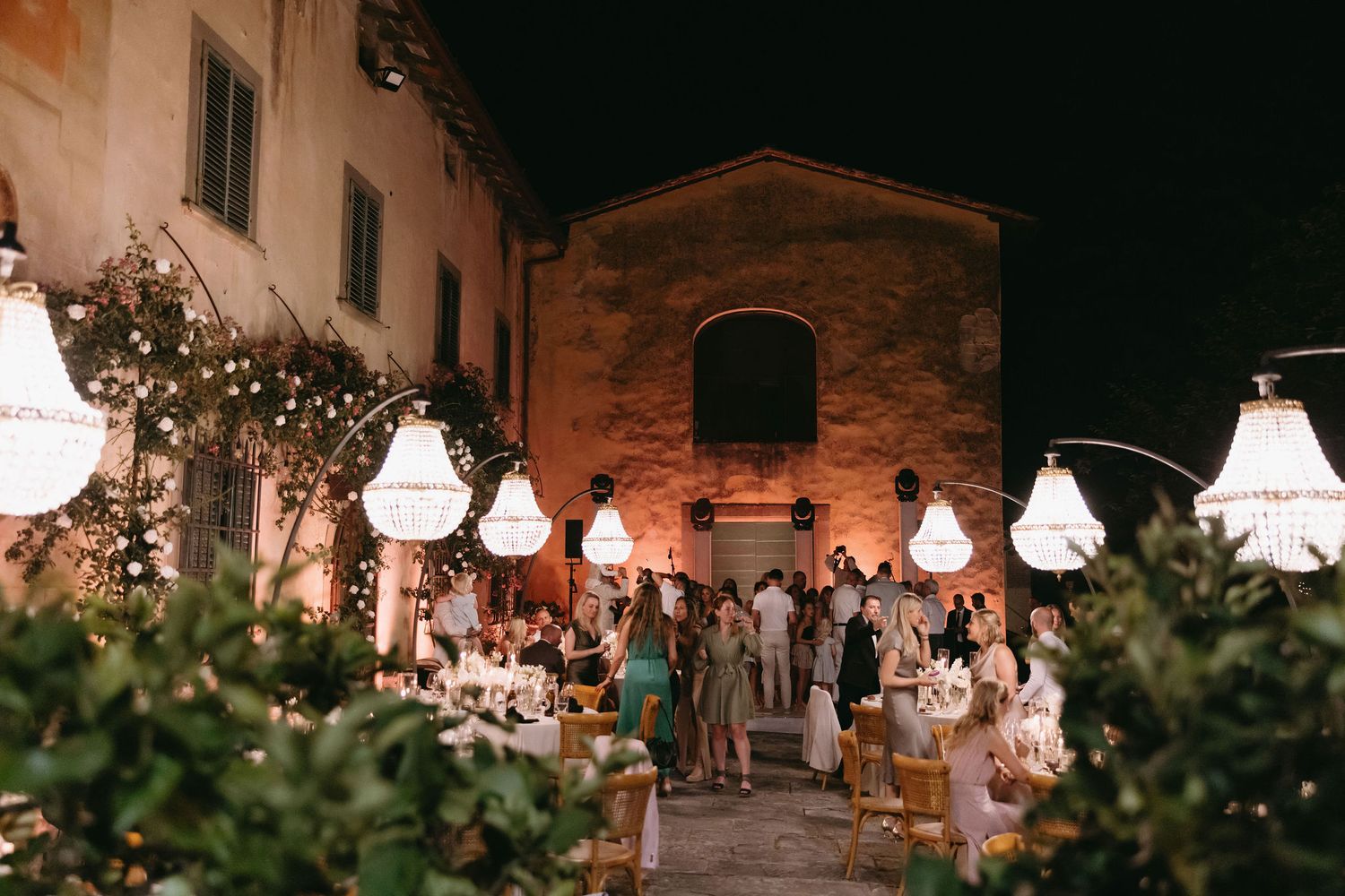 Evening wedding celebration with hanging lanterns illuminating a rustic Italian courtyard.