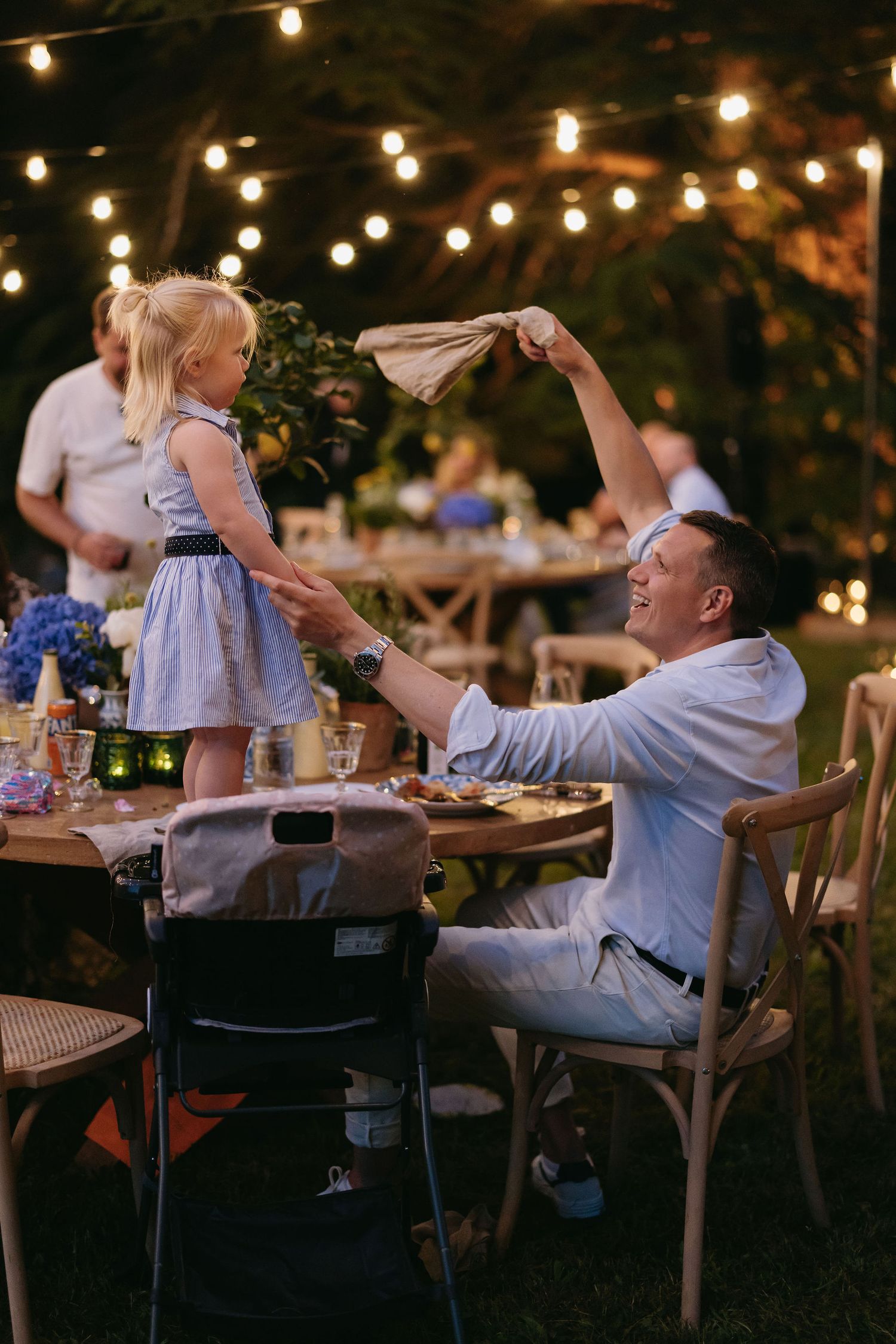 Evening outdoor reception with string lights where guests celebrate at tables.