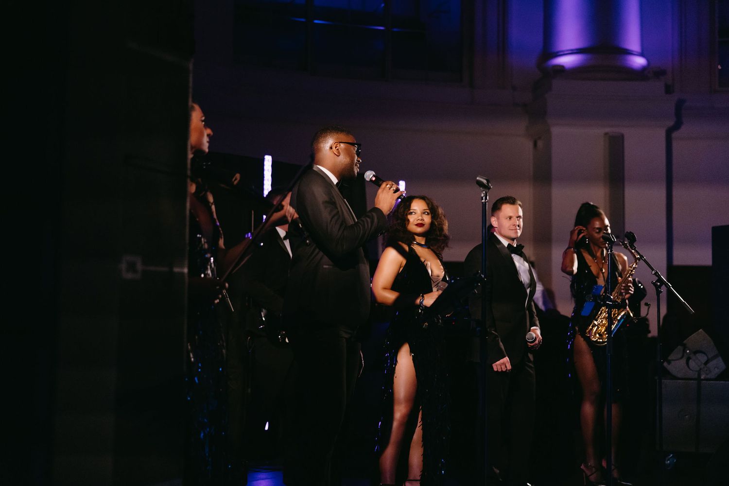 Wedding band performs on stage with singers in formal attire under purple lighting.