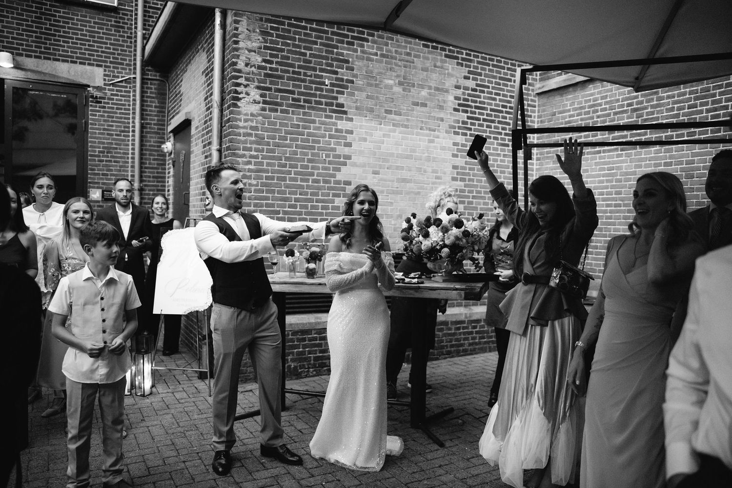 Black and white photo of wedding guests mingling outside brick building.