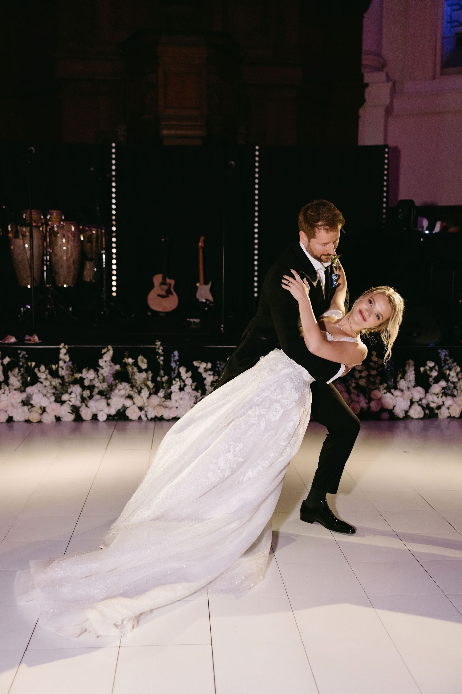 Dramatic first dance on white dance floor with stunning dip move and floral decorations.