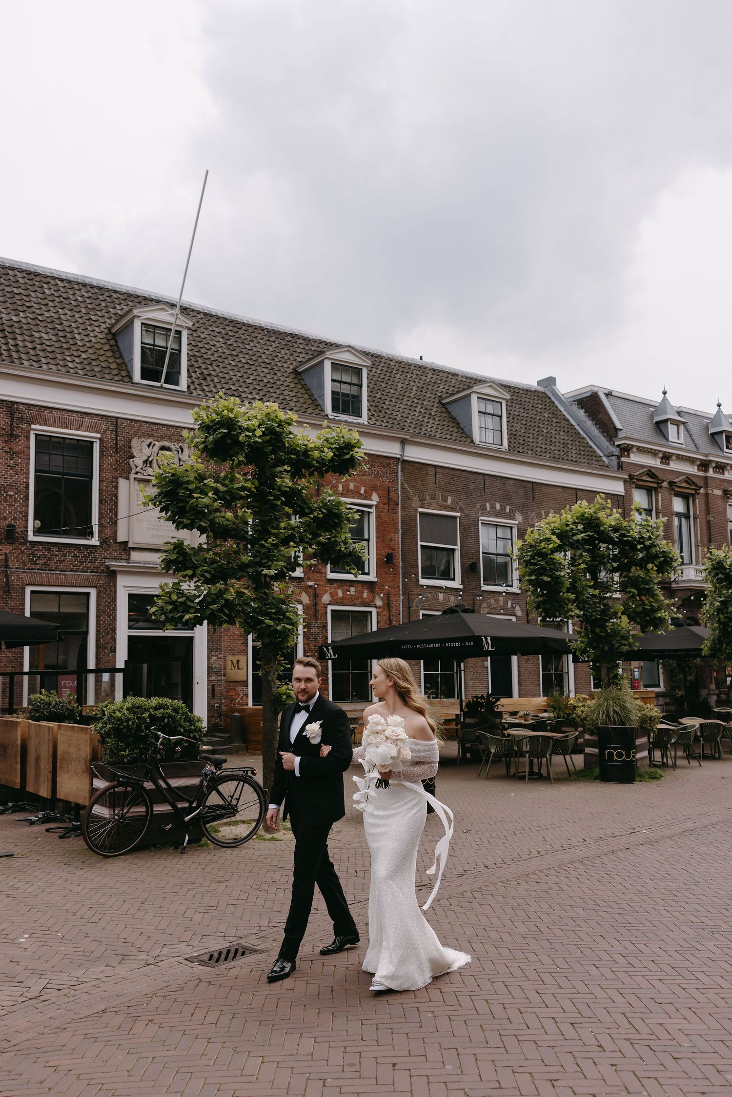 A couple walks together on a cobblestone street in front of classic Dutch architecture.