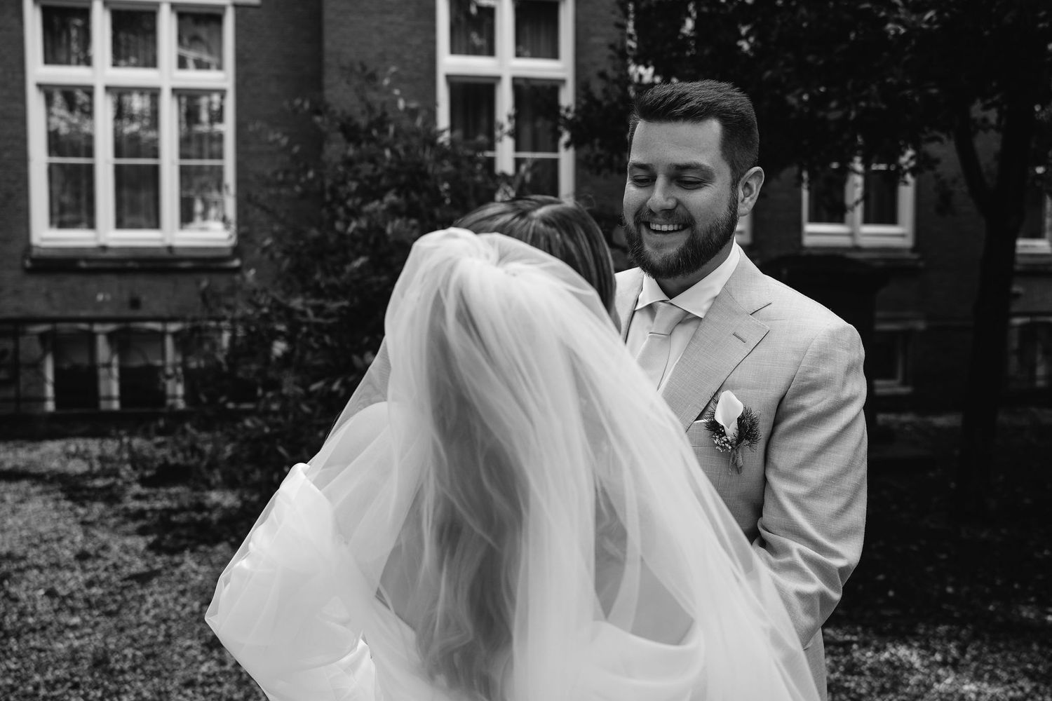Black and white candid moment between newlyweds sharing laughter outdoors.