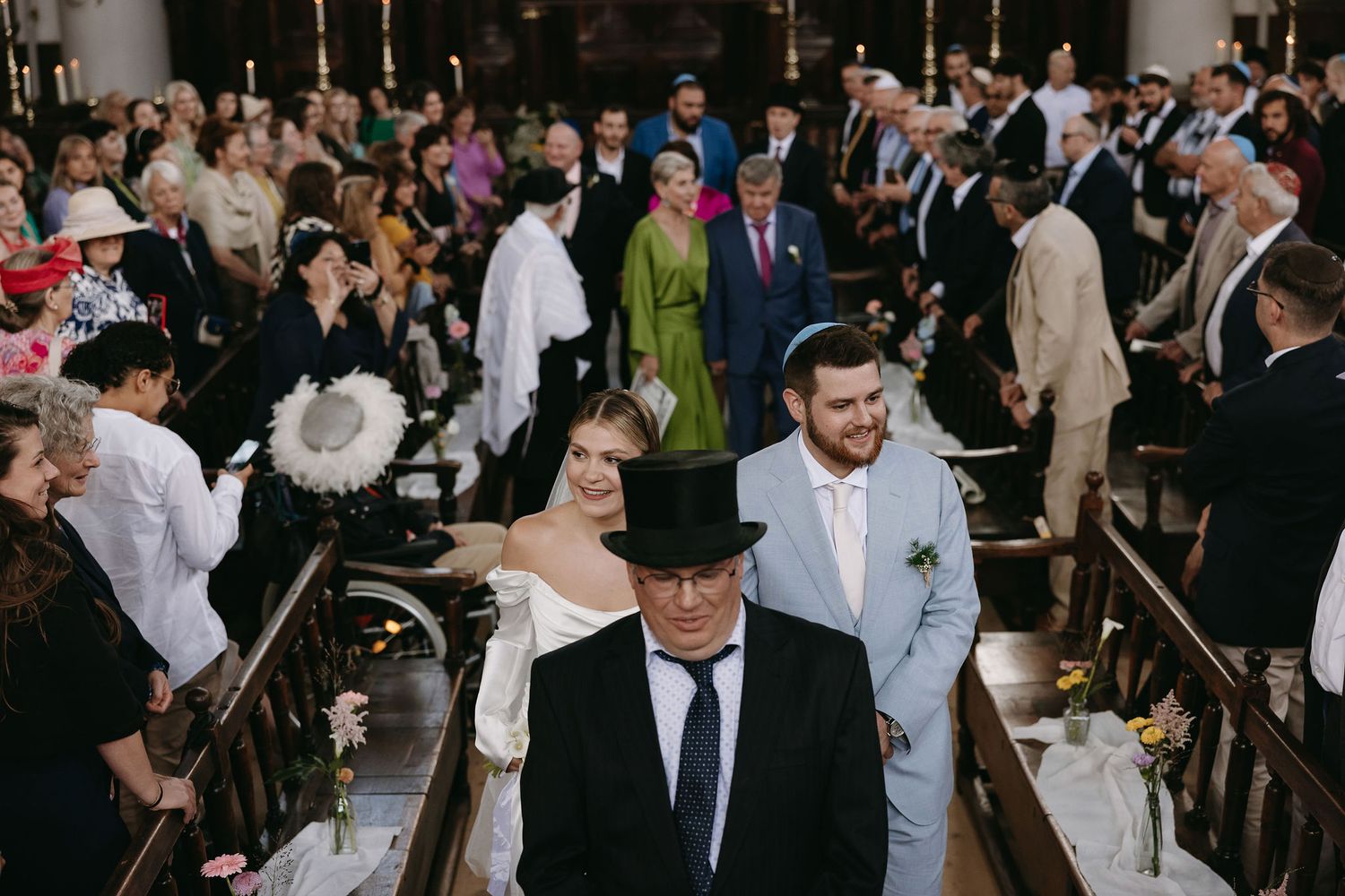 Wedding ceremony guests gathered in a church with ornate chandeliers and traditional decor.