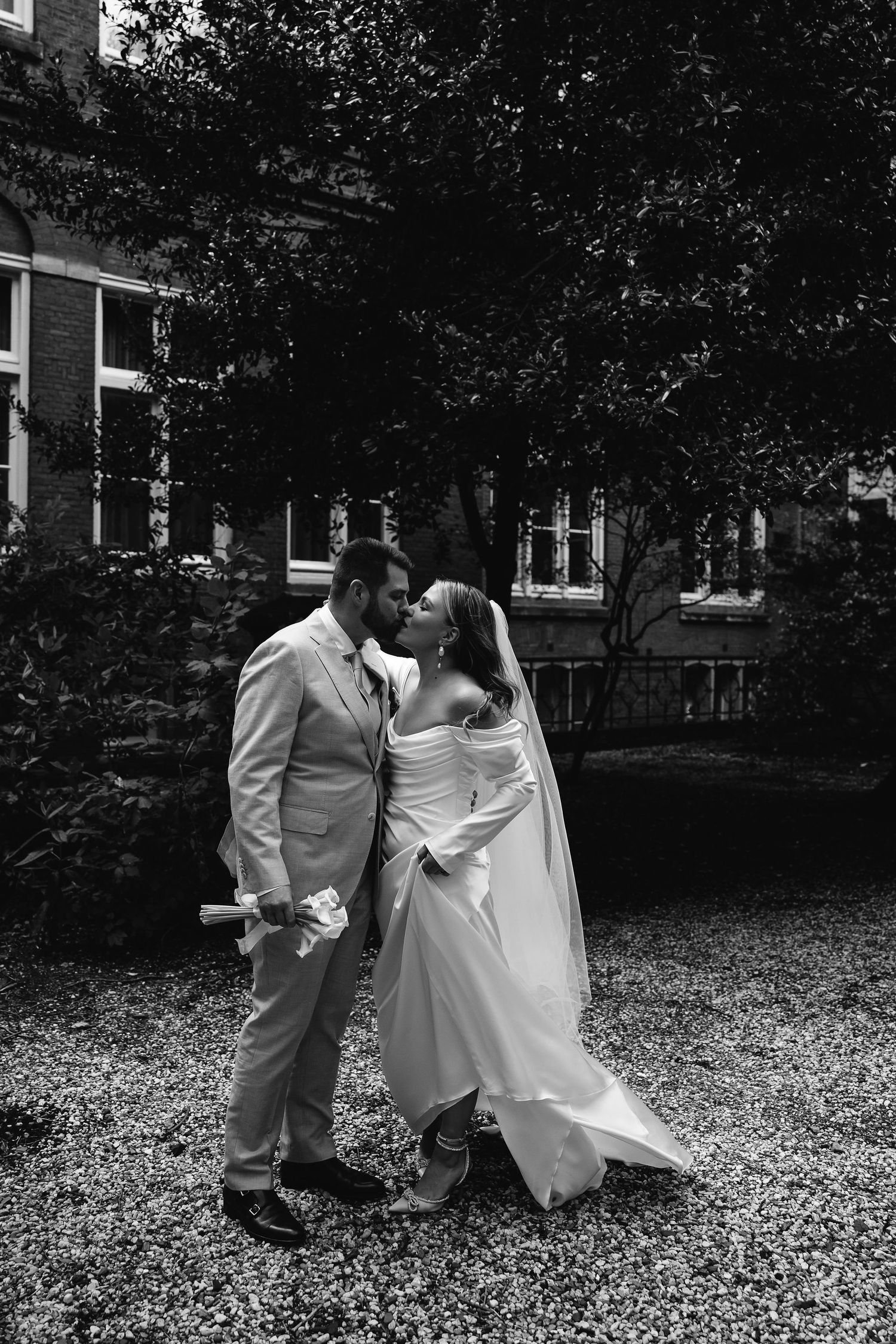 Black and white wedding photo captured outdoors among trees and fallen leaves.