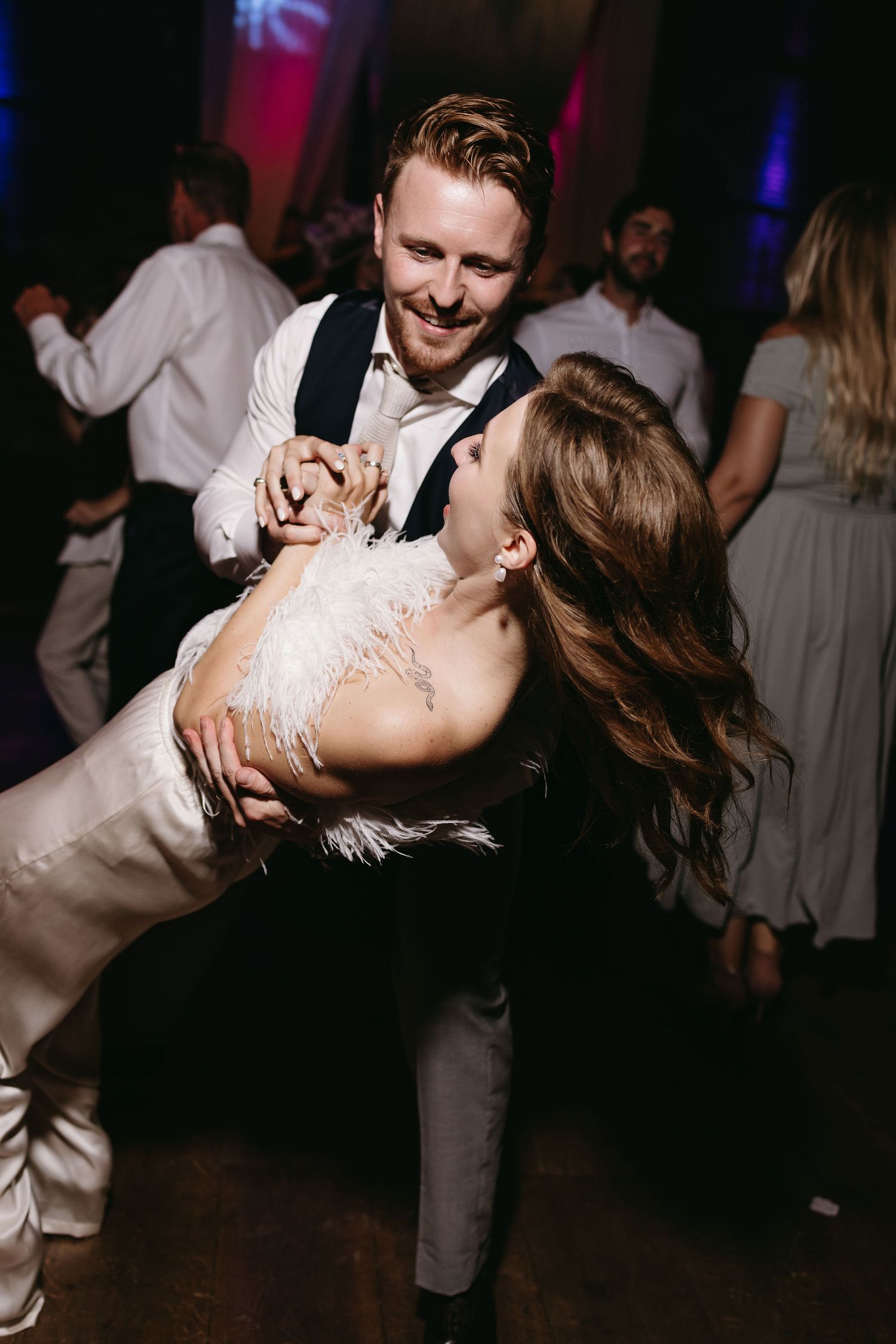 A couple dances together at their wedding reception as the groom dips his bride in an elegant white feathered gown.