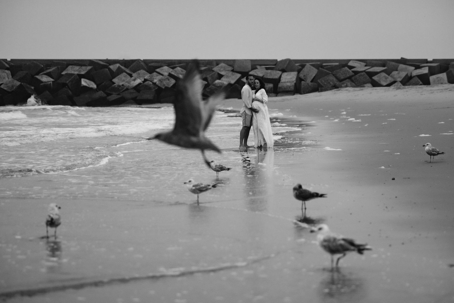 Black and white beach scene with seagulls and distant figures by the water.
