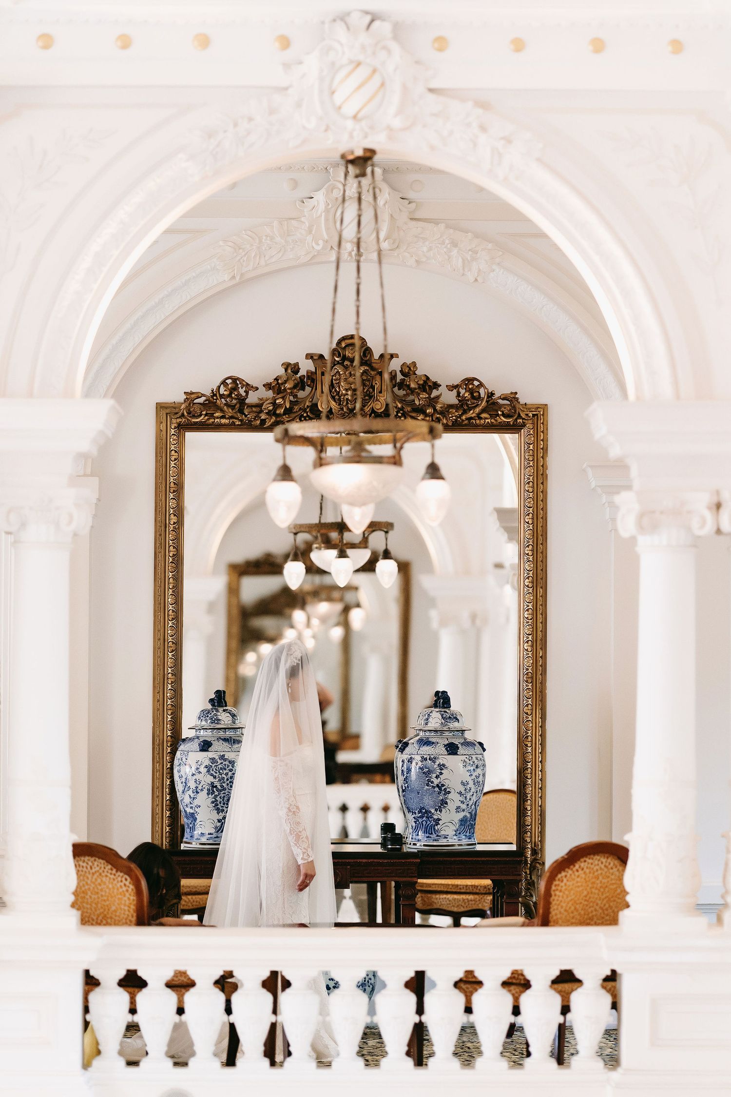 An elegant white archway with chandeliers, ornate mirrors and blue vases displayed in a classic interior.