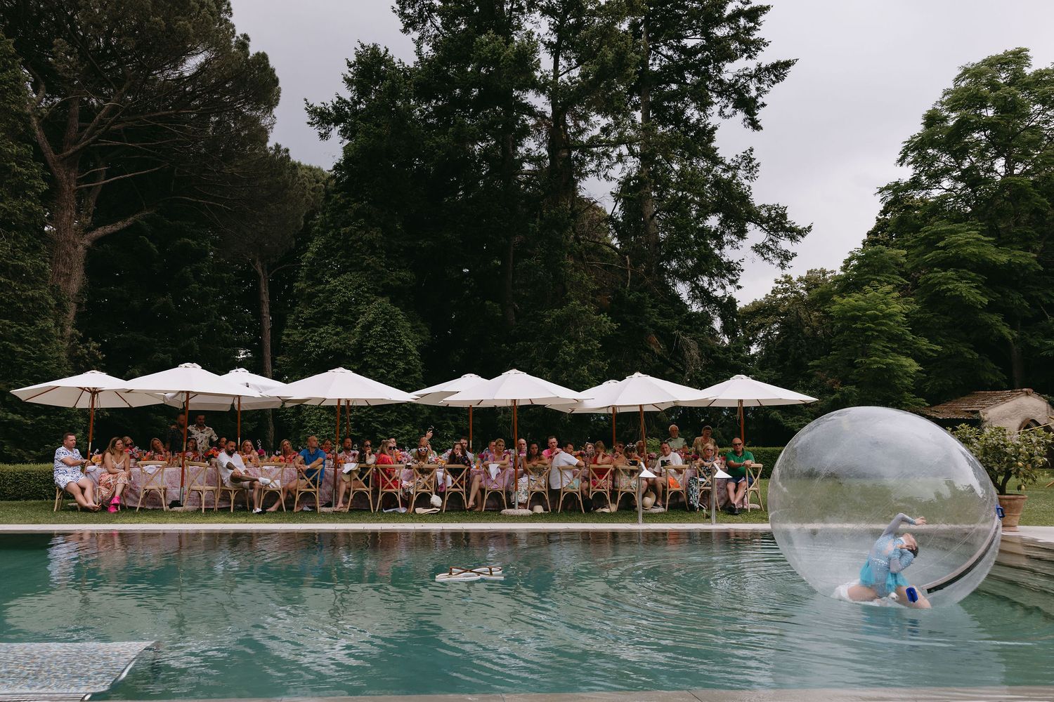Pool party celebration with white umbrellas and large transparent bubble on the water.