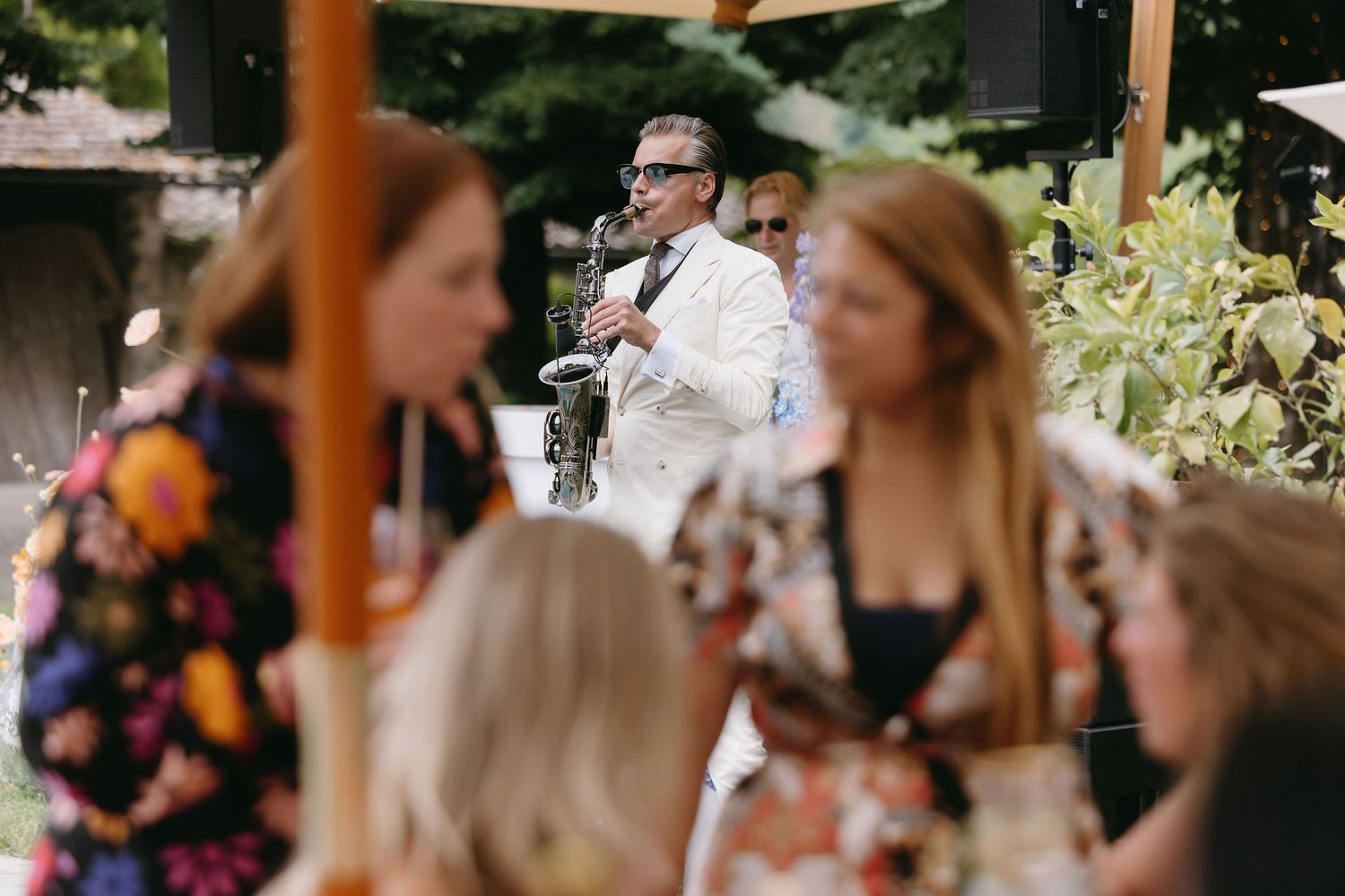 Casual outdoor garden party with guests enjoying refreshments under umbrellas.