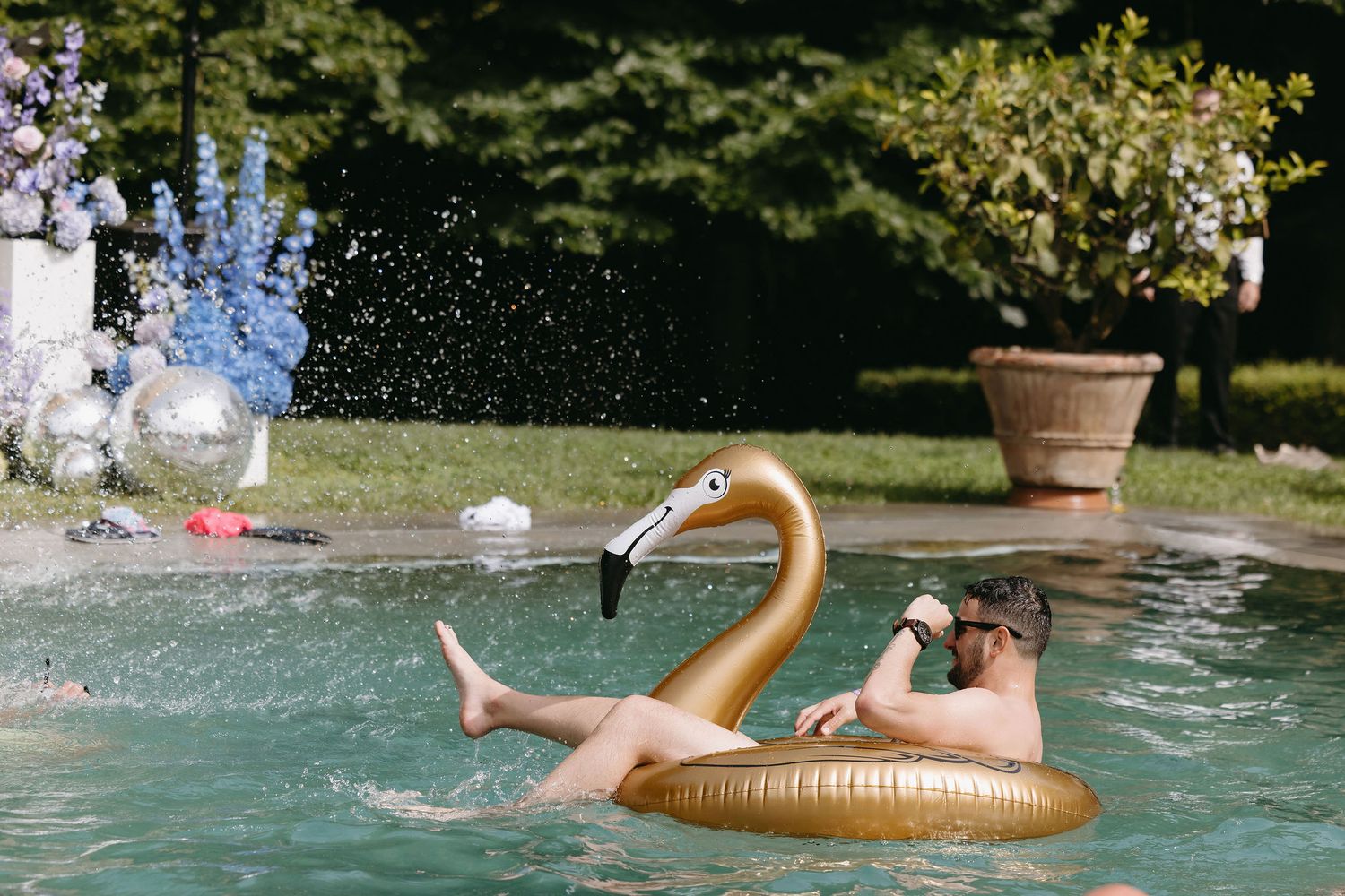 Person splashing in a pool with a golden swan float on a sunny day.