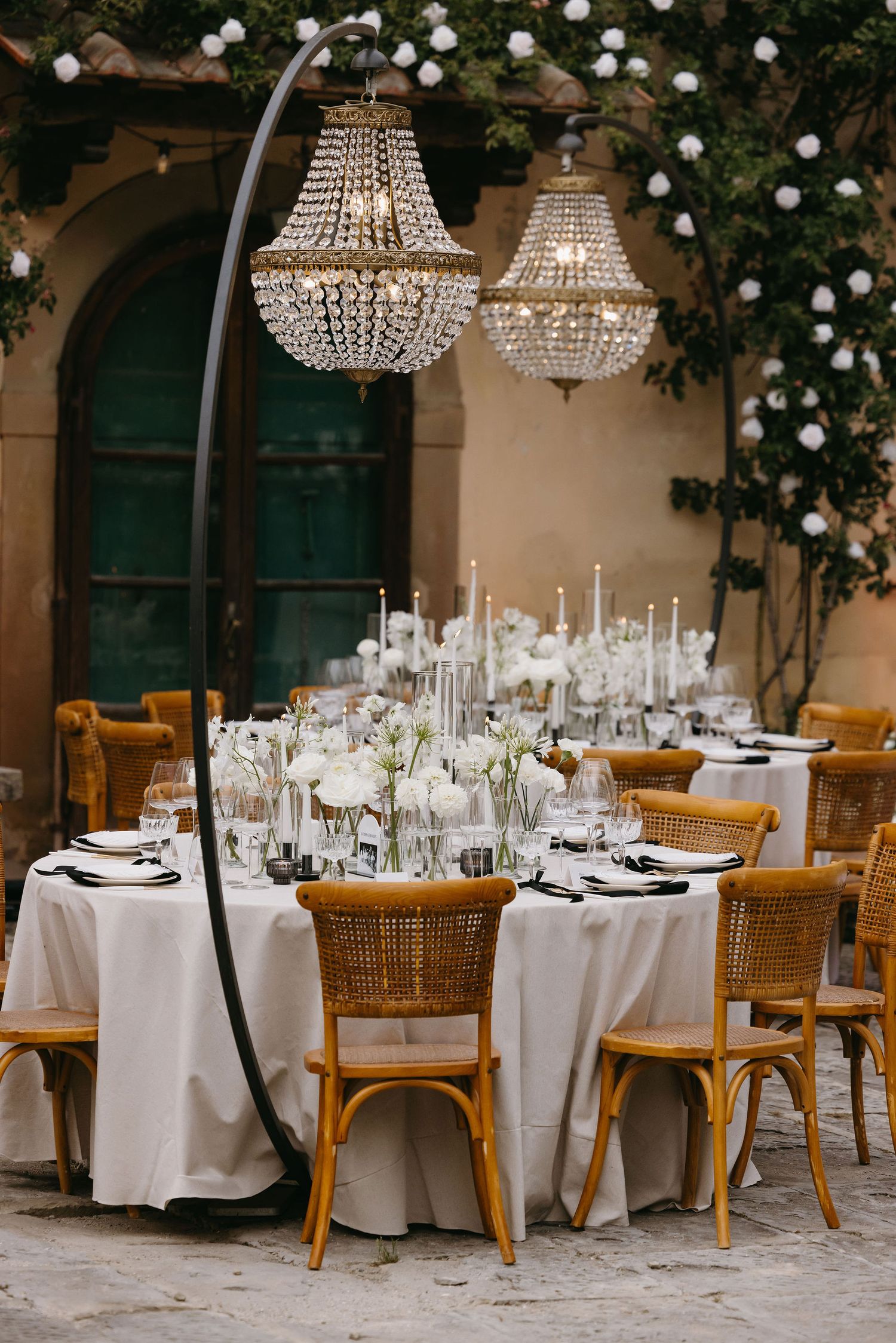 Elegant outdoor wedding table setting with crystal chandeliers and bistro chairs.