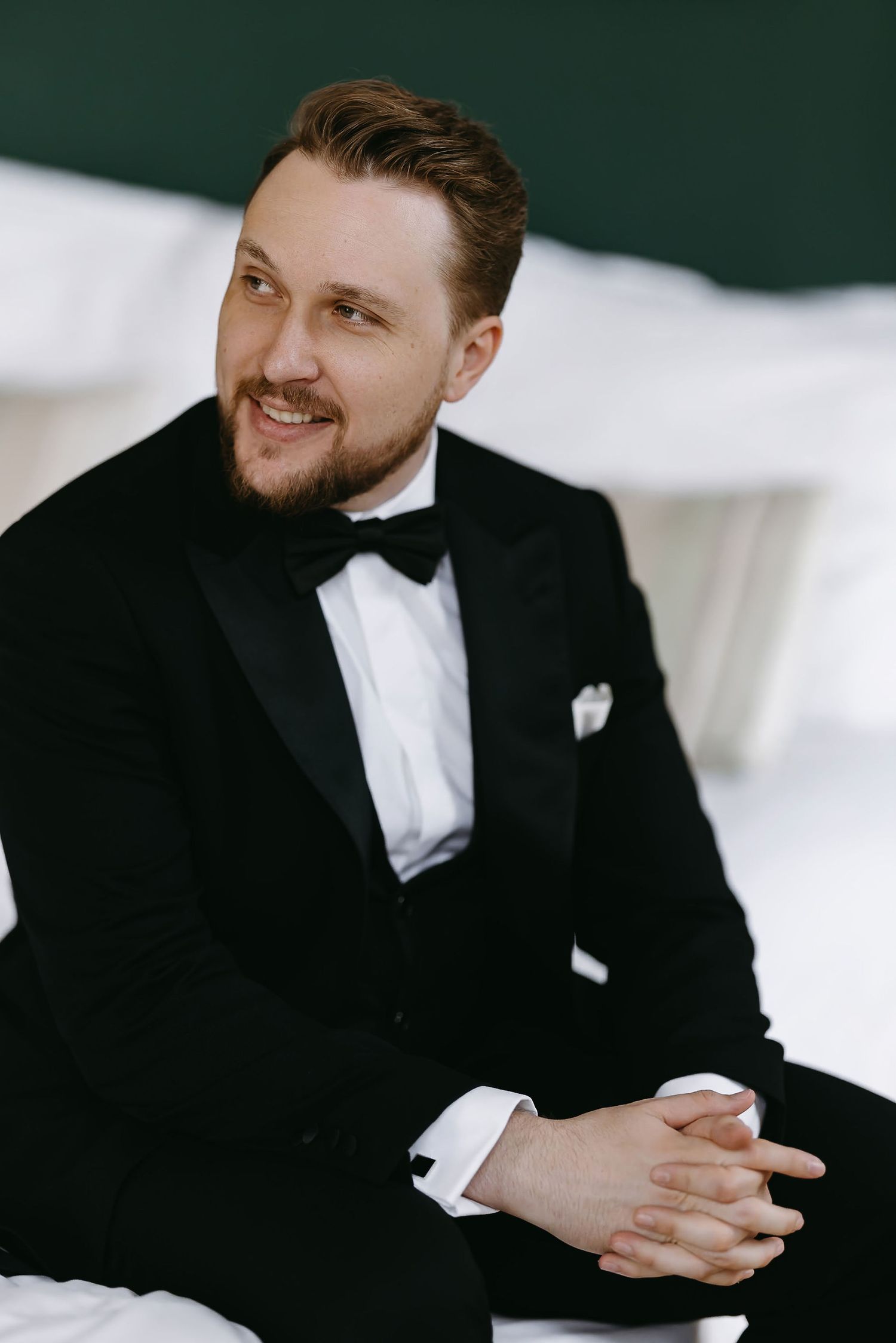 Elegant groom in black tuxedo and bowtie sitting and smiling.