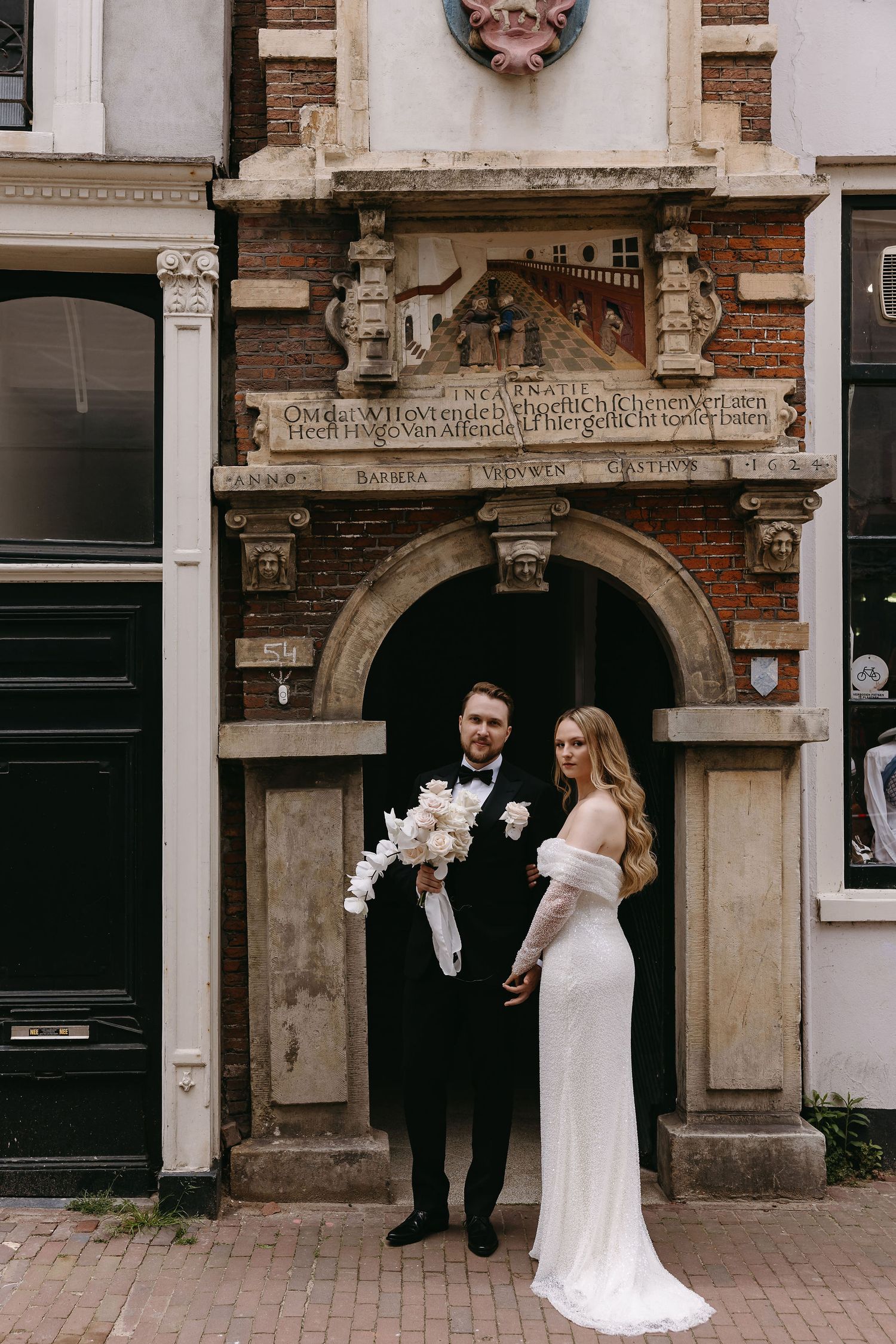 A couple poses in wedding attire beneath an ornate historic archway with architectural details.