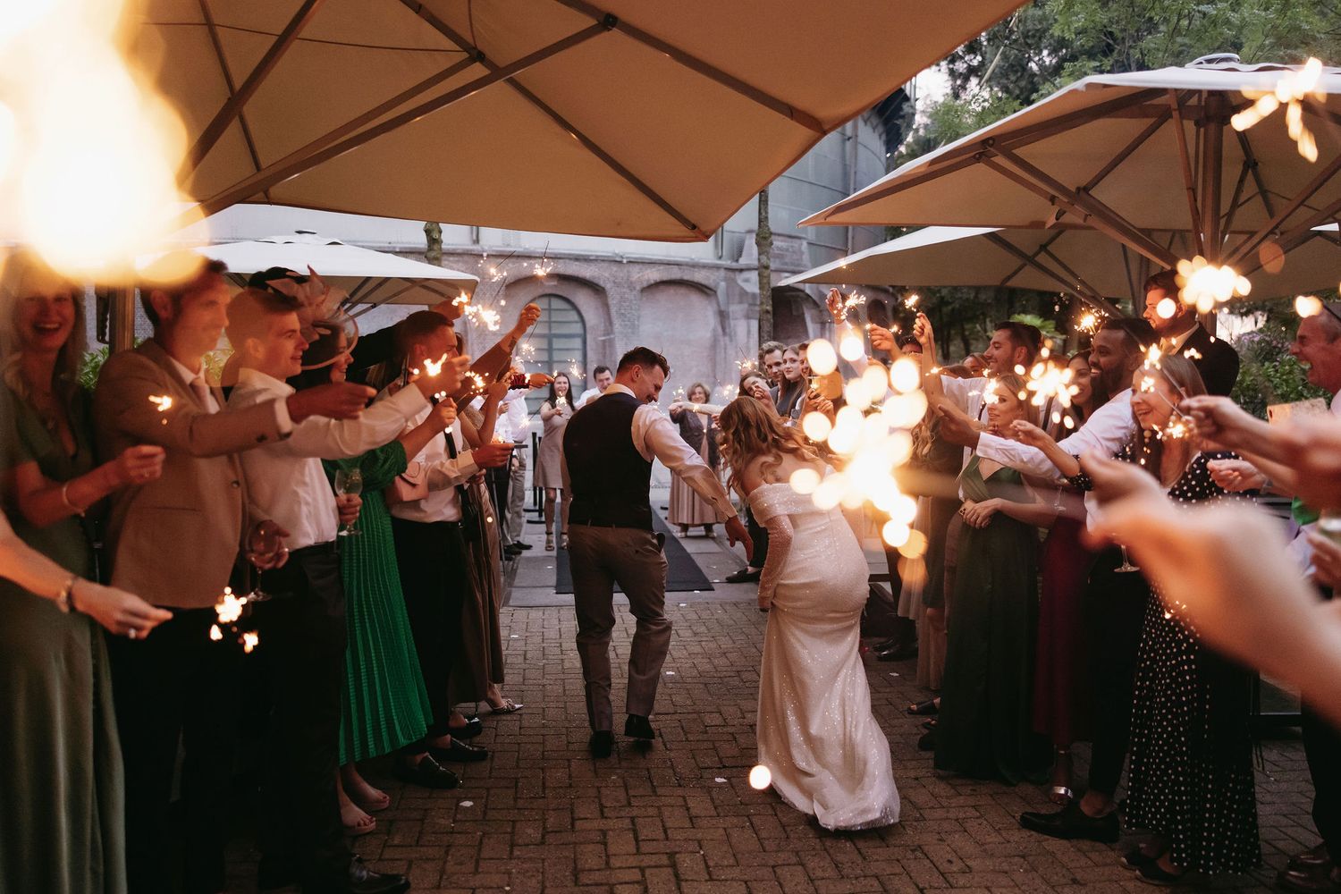 Wedding party dancing under outdoor umbrellas and string lights at dusk.