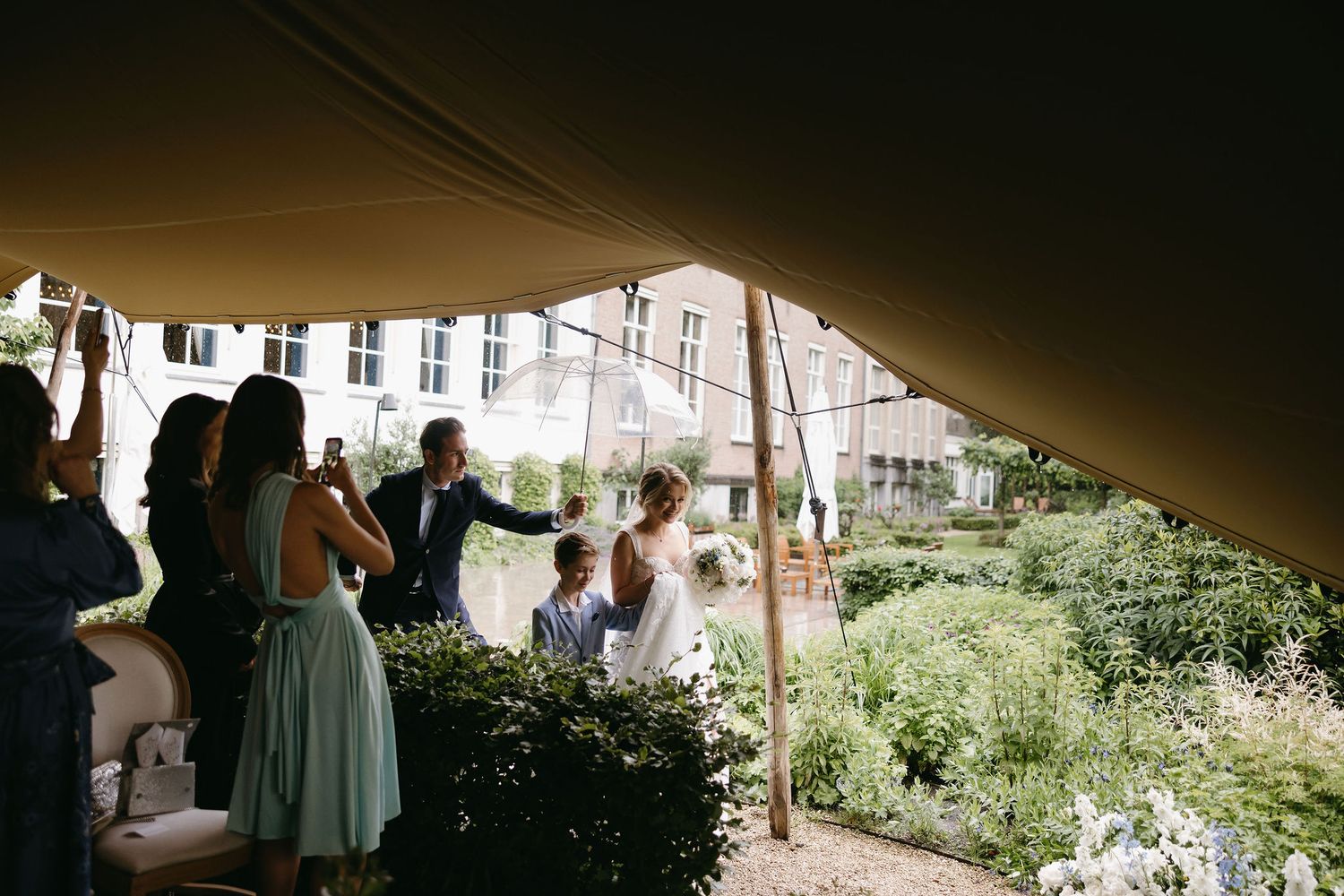 Wedding guests mingling under a tent canopy during an outdoor garden reception.