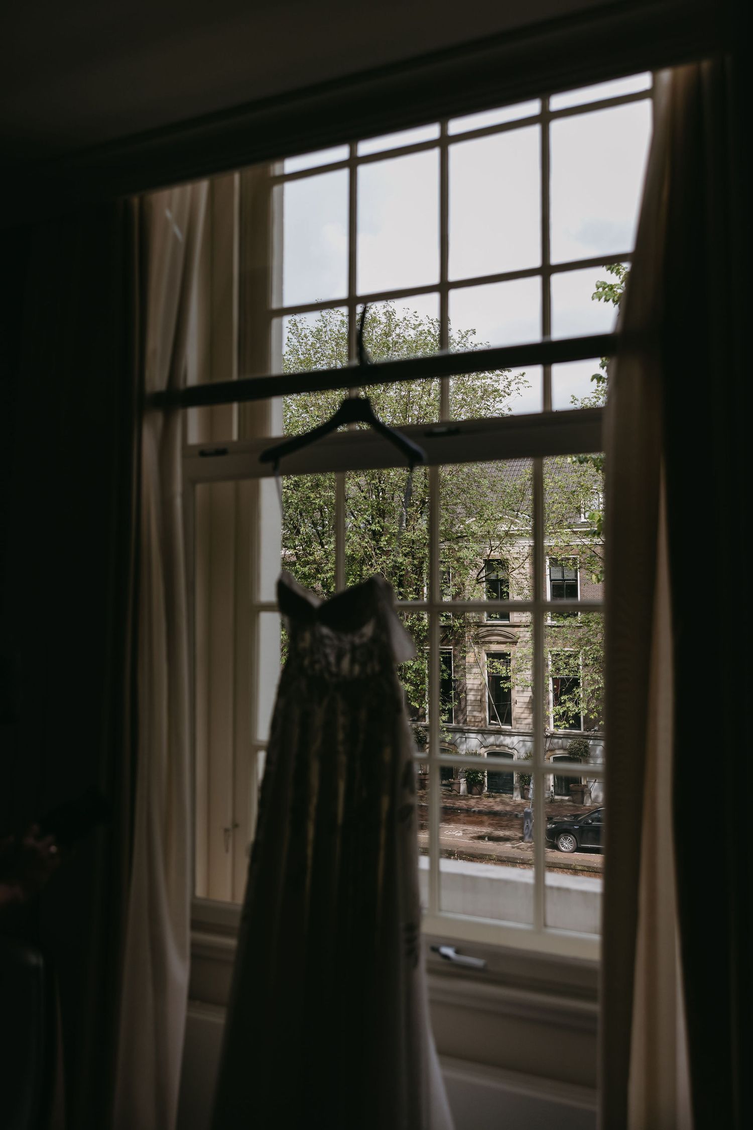 Series of dark silhouettes showing a dress hanging by large windows with natural light.