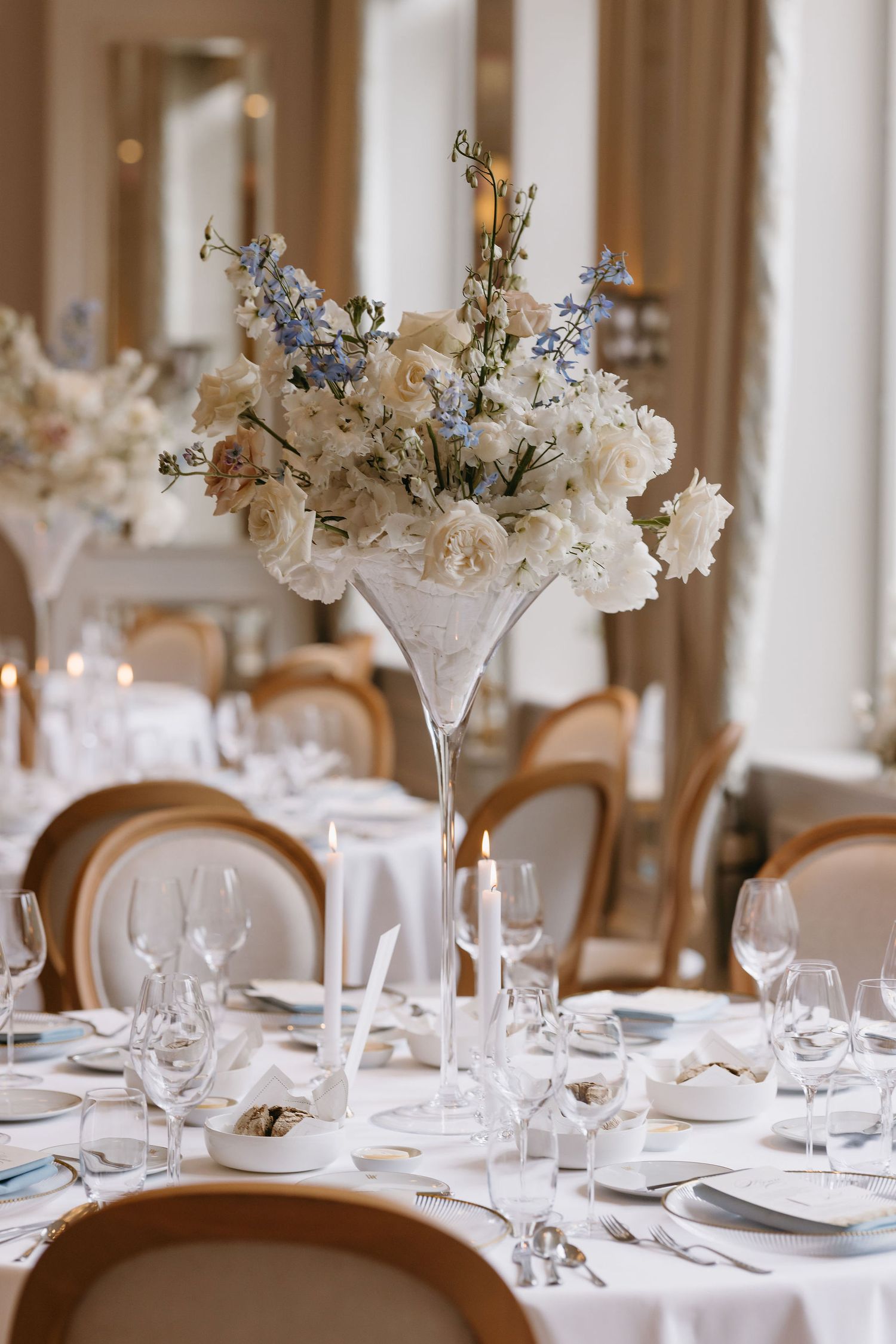 Elegant wedding table centerpiece with white flowers in martini glass vase surrounded by wine glasses.