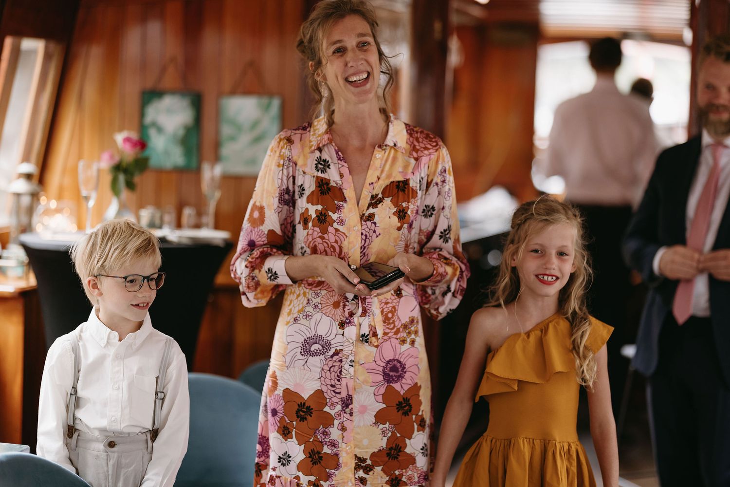 A joyful moment at a wedding celebration showing people in formal attire including a floral dress and children's formalwear.