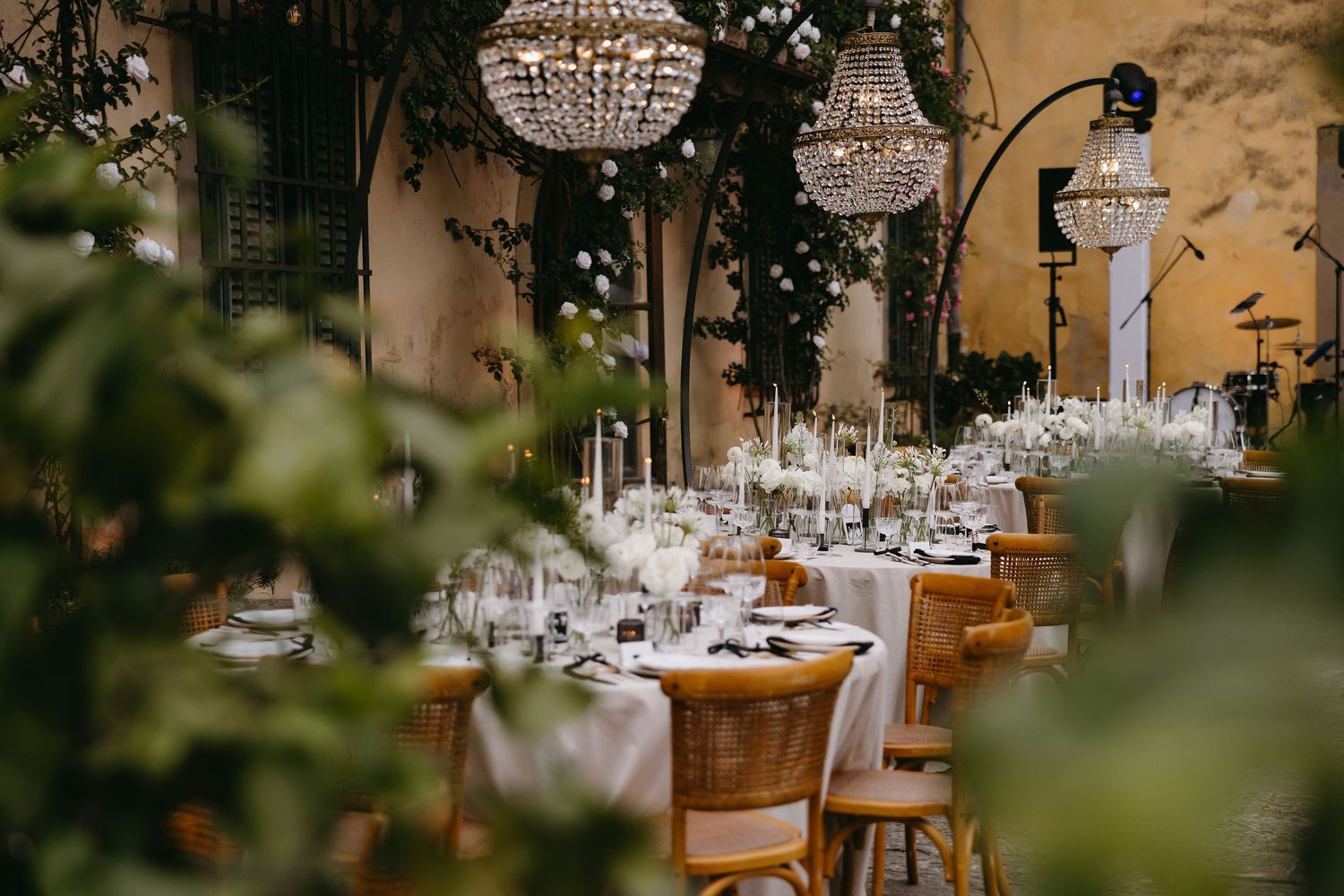 Elegant outdoor wedding reception tables decorated with crystal chandeliers and lush greenery.