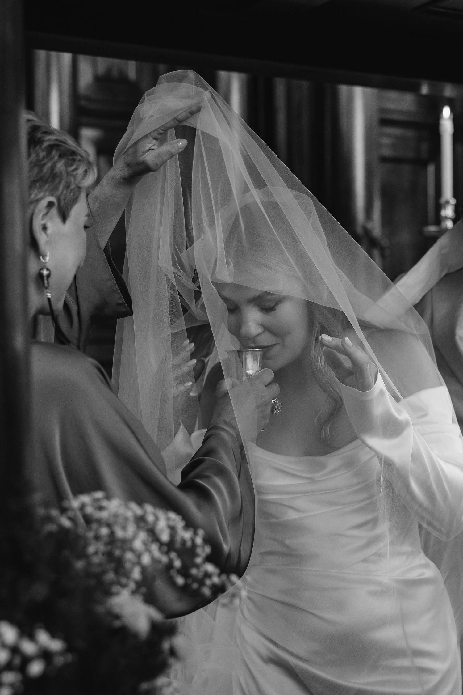 A candid black and white moment of a bride adjusting her veil during wedding preparations.