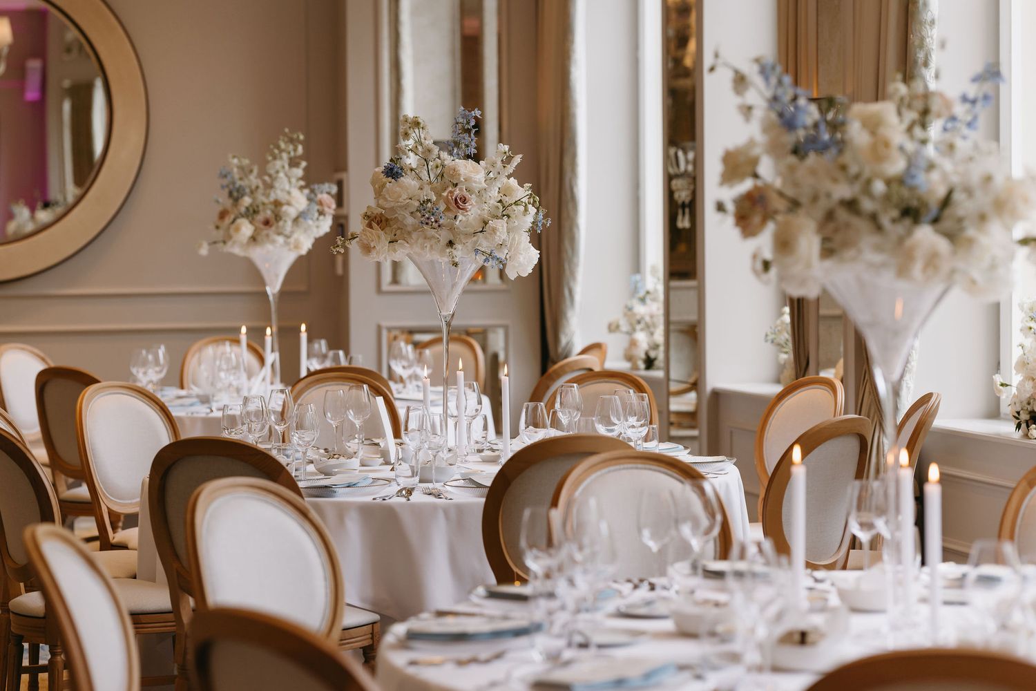 Elegant wedding reception tables set with fine china and crystal glassware under ornate chandeliers.