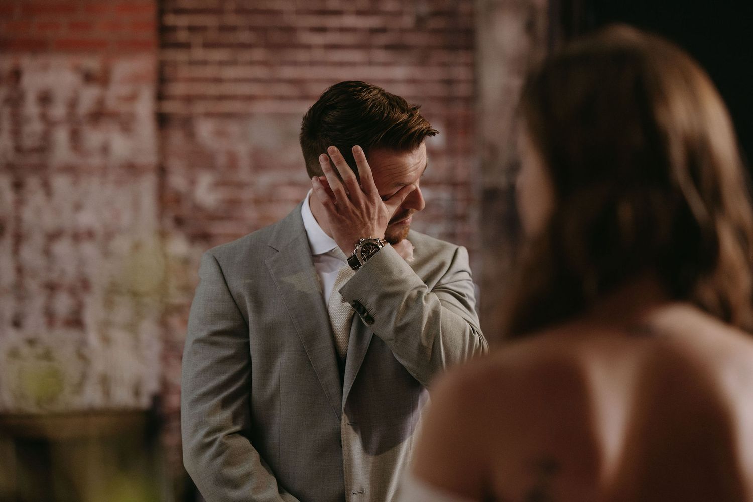Emotional wedding moment captured against exposed brick wall background.