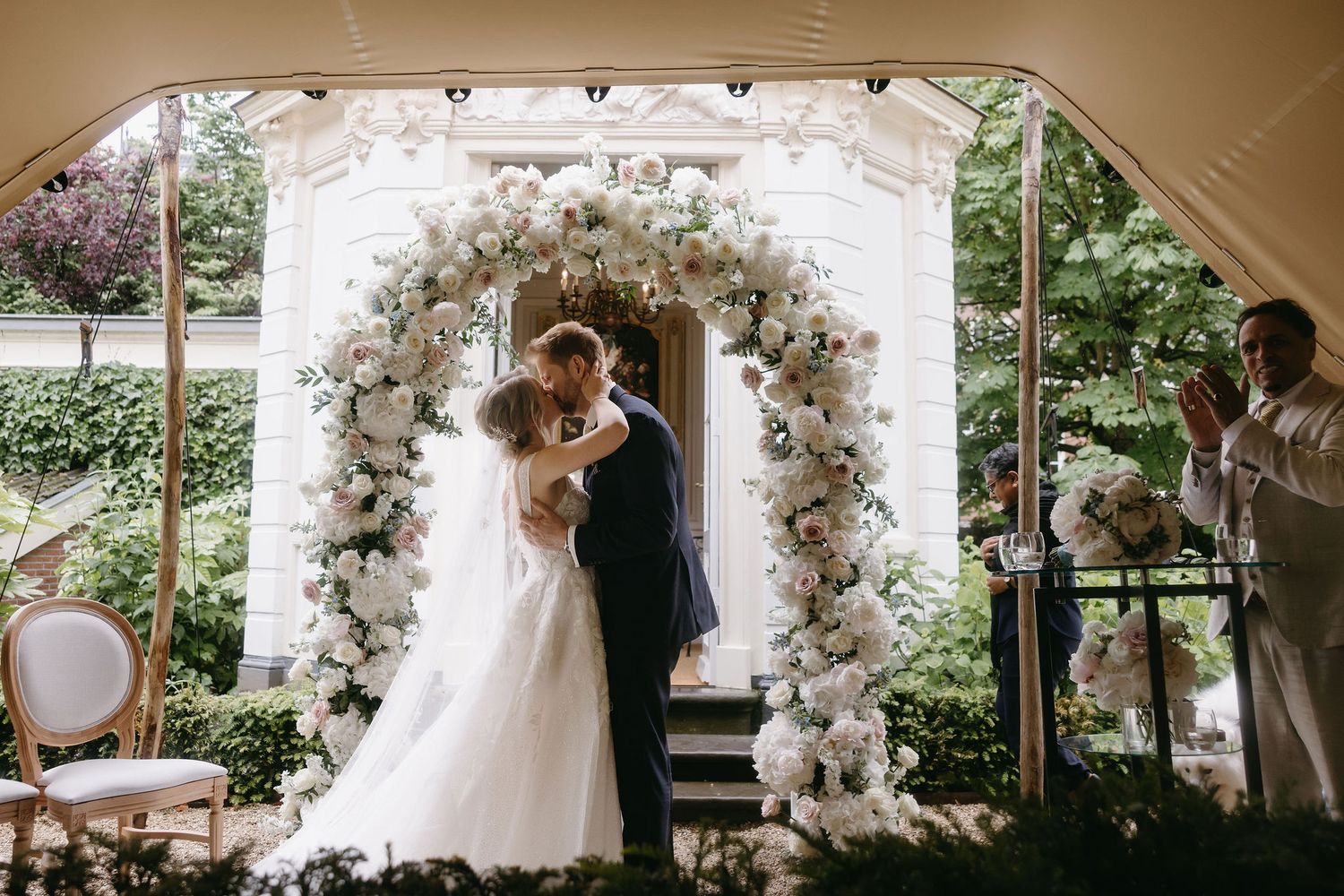 Wedding ceremony under a floral arch outdoors with white and blush roses.
