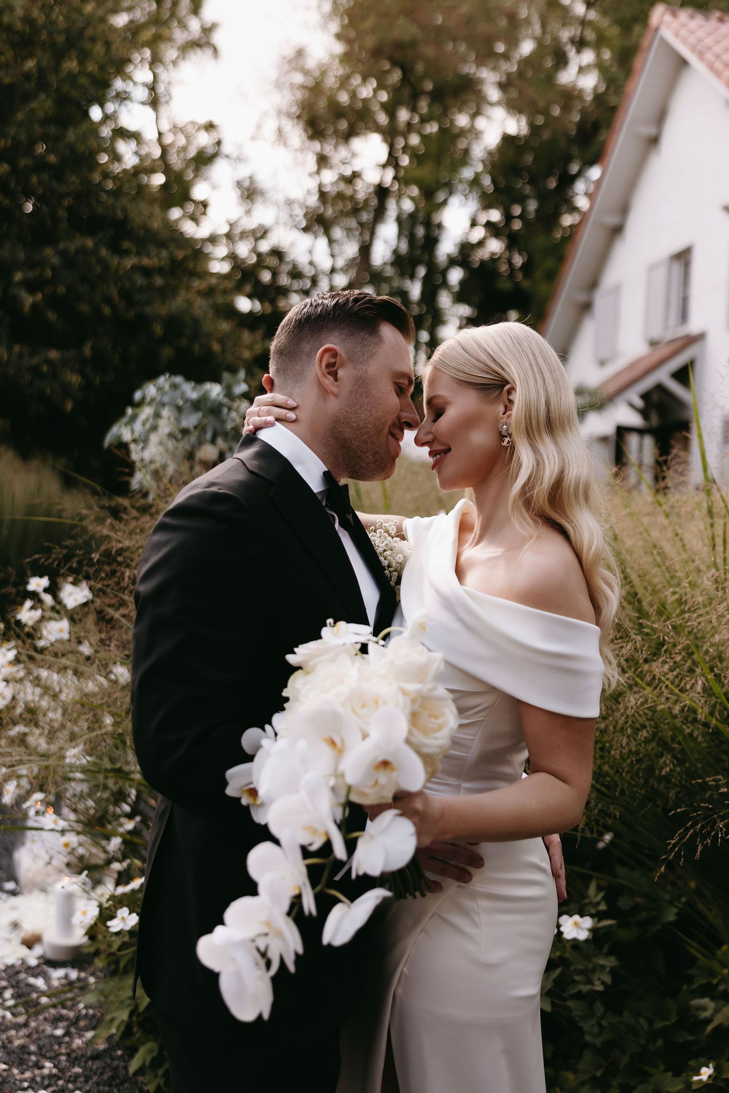 Intimate wedding portrait with white orchid bouquet in an outdoor garden setting.