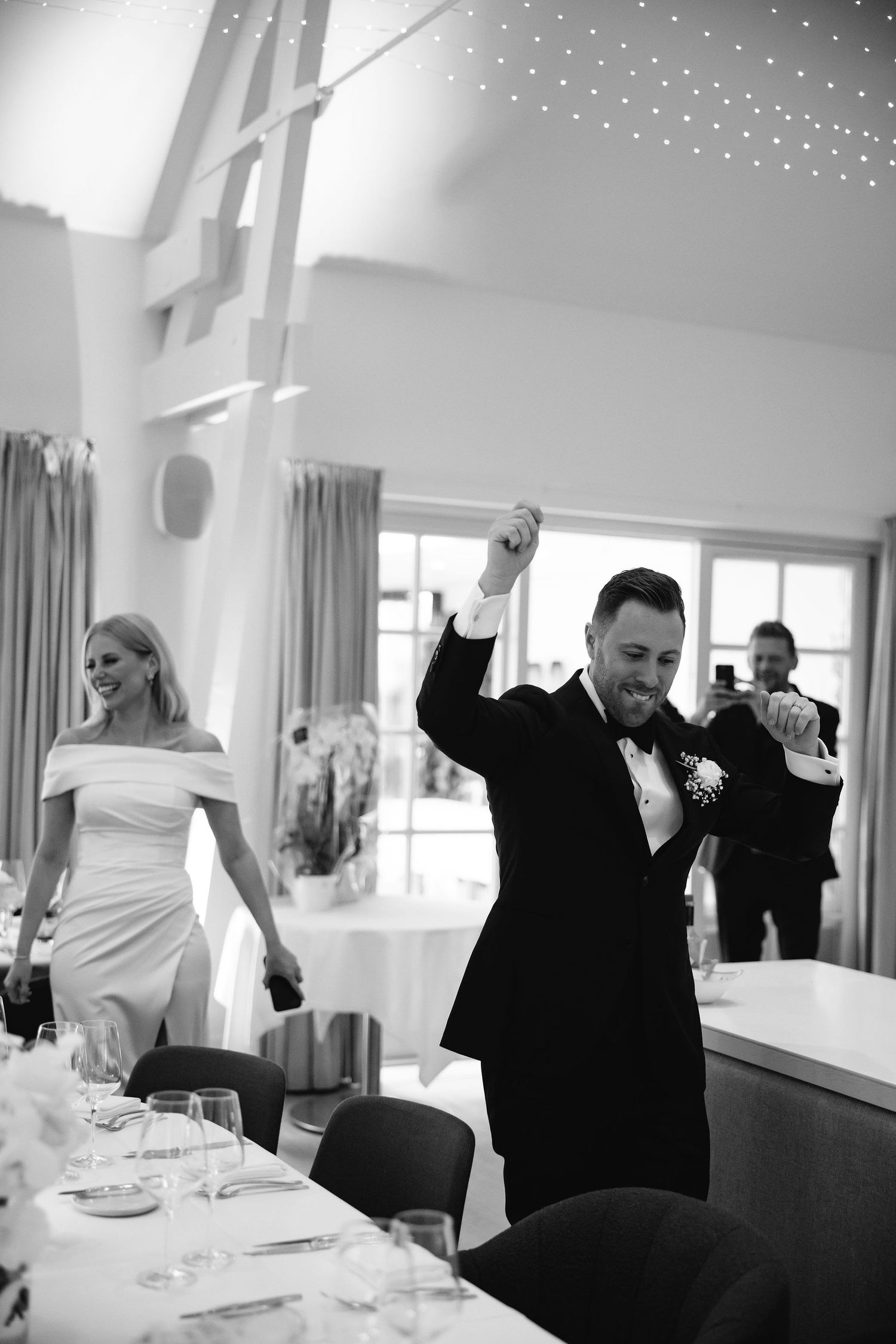 Black and white photo of wedding celebration with guests celebrating at reception tables.