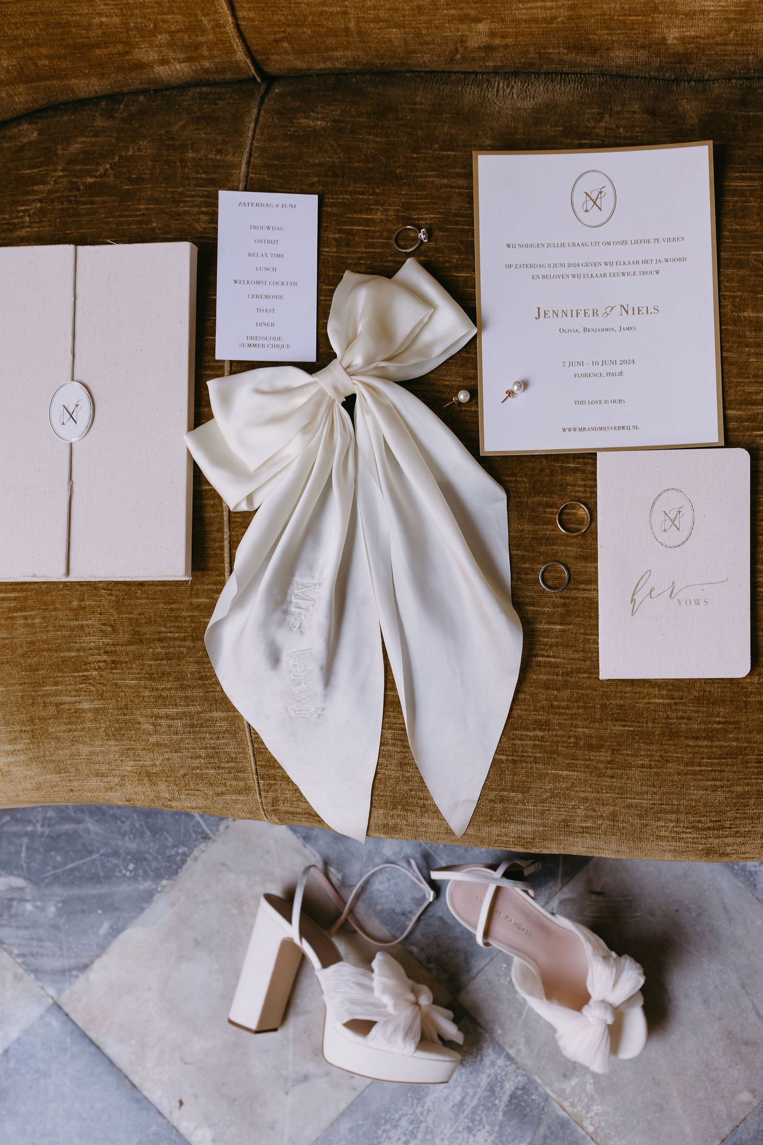 Elegant wedding stationery with white bow and bridal shoes arranged on wooden surface.