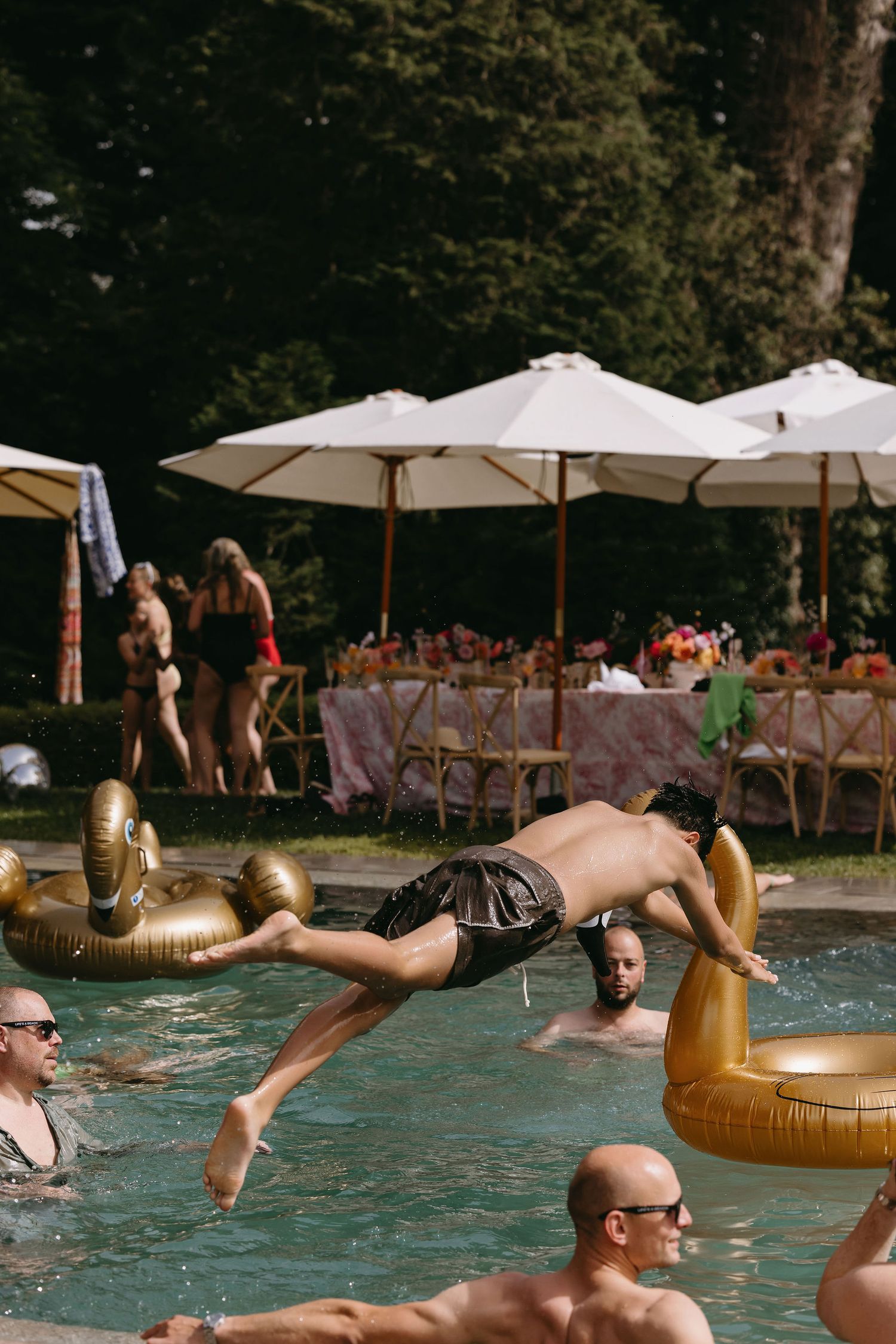 Wedding guests enjoy a pool party with gold inflatable floats in the water.