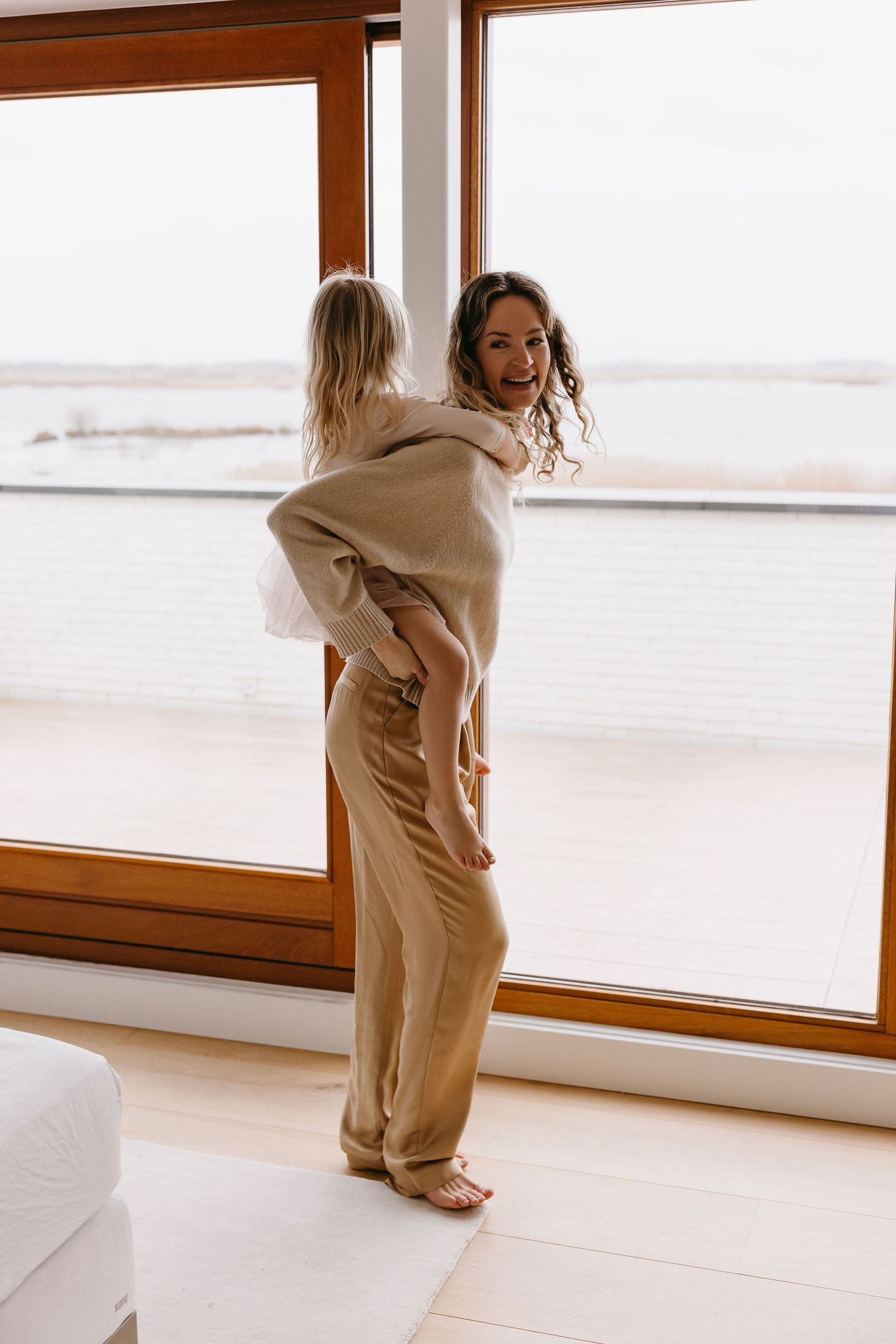 A joyful piggyback ride moment in a sun-filled room with large windows.