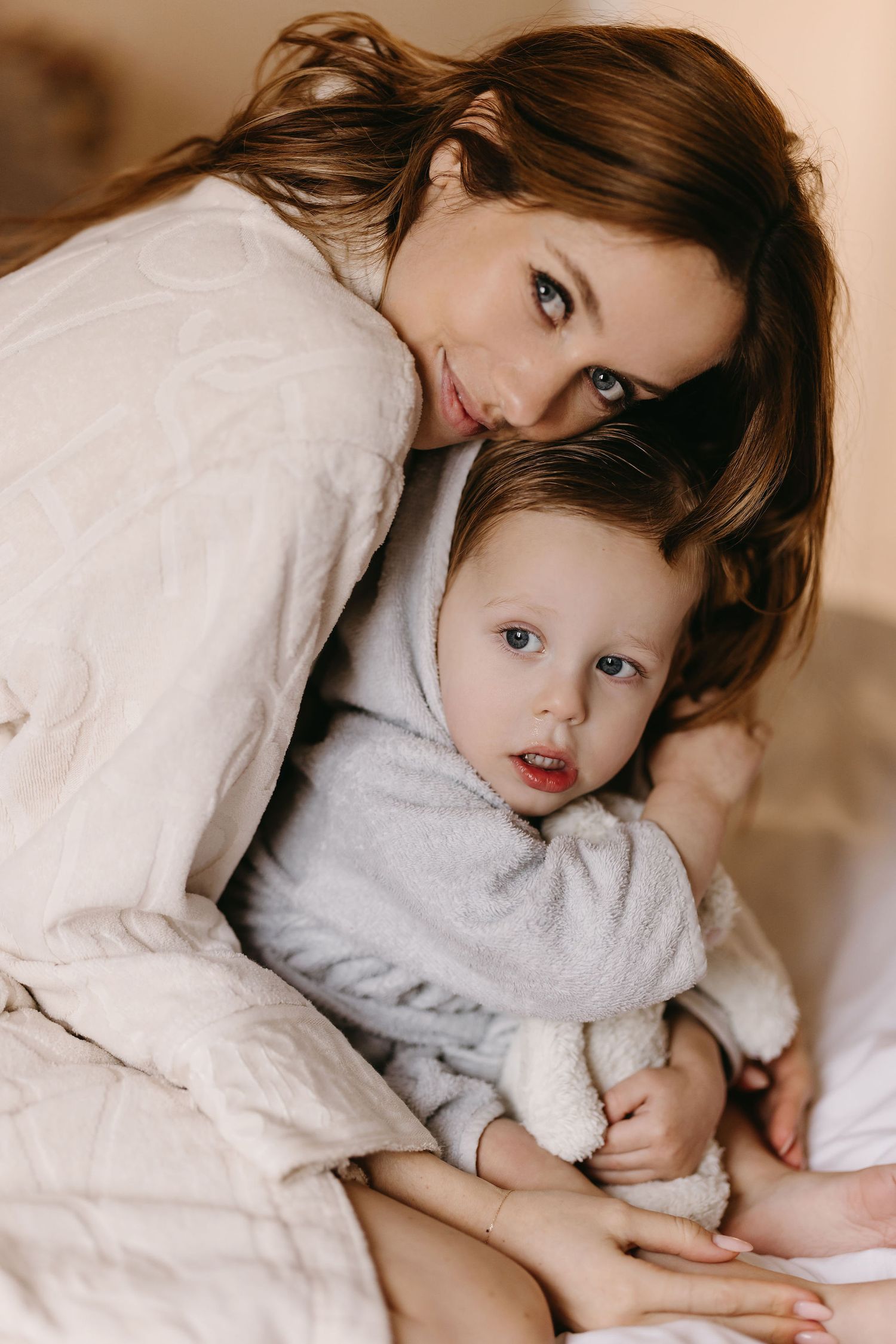 An intimate portrait of parent and child snuggling together on white bedding.