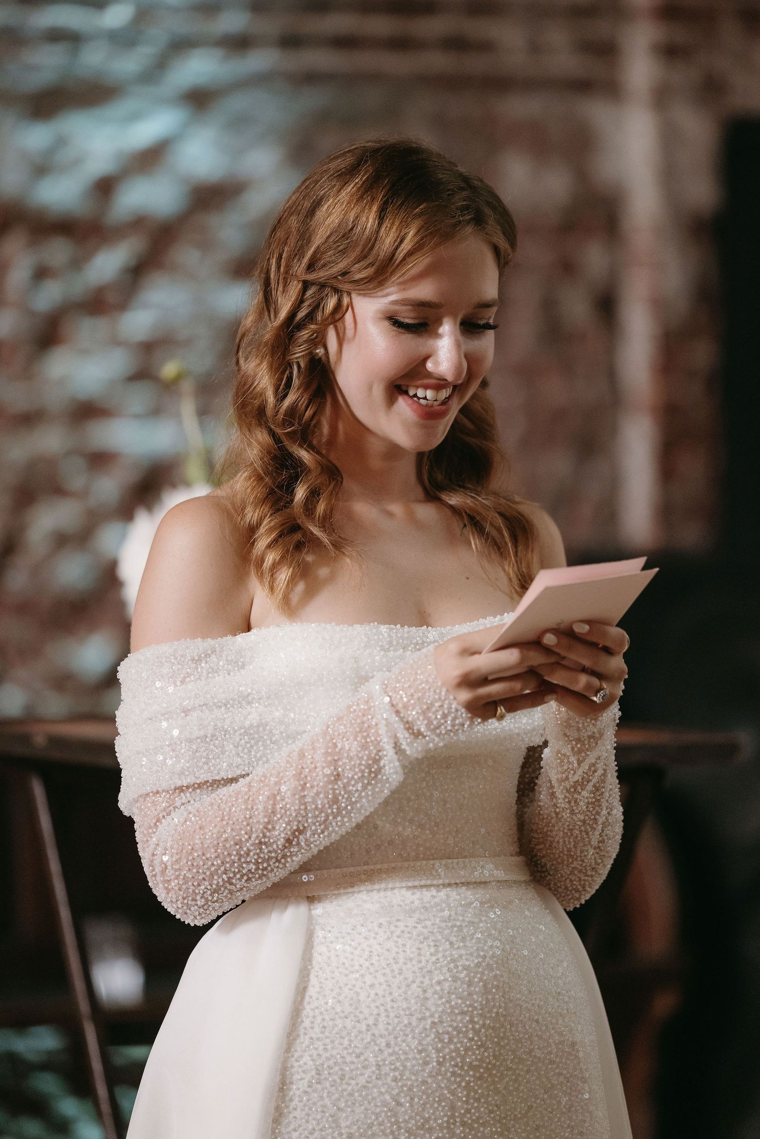 The off-shoulder beaded details of a romantic wedding gown sparkle in soft lighting.