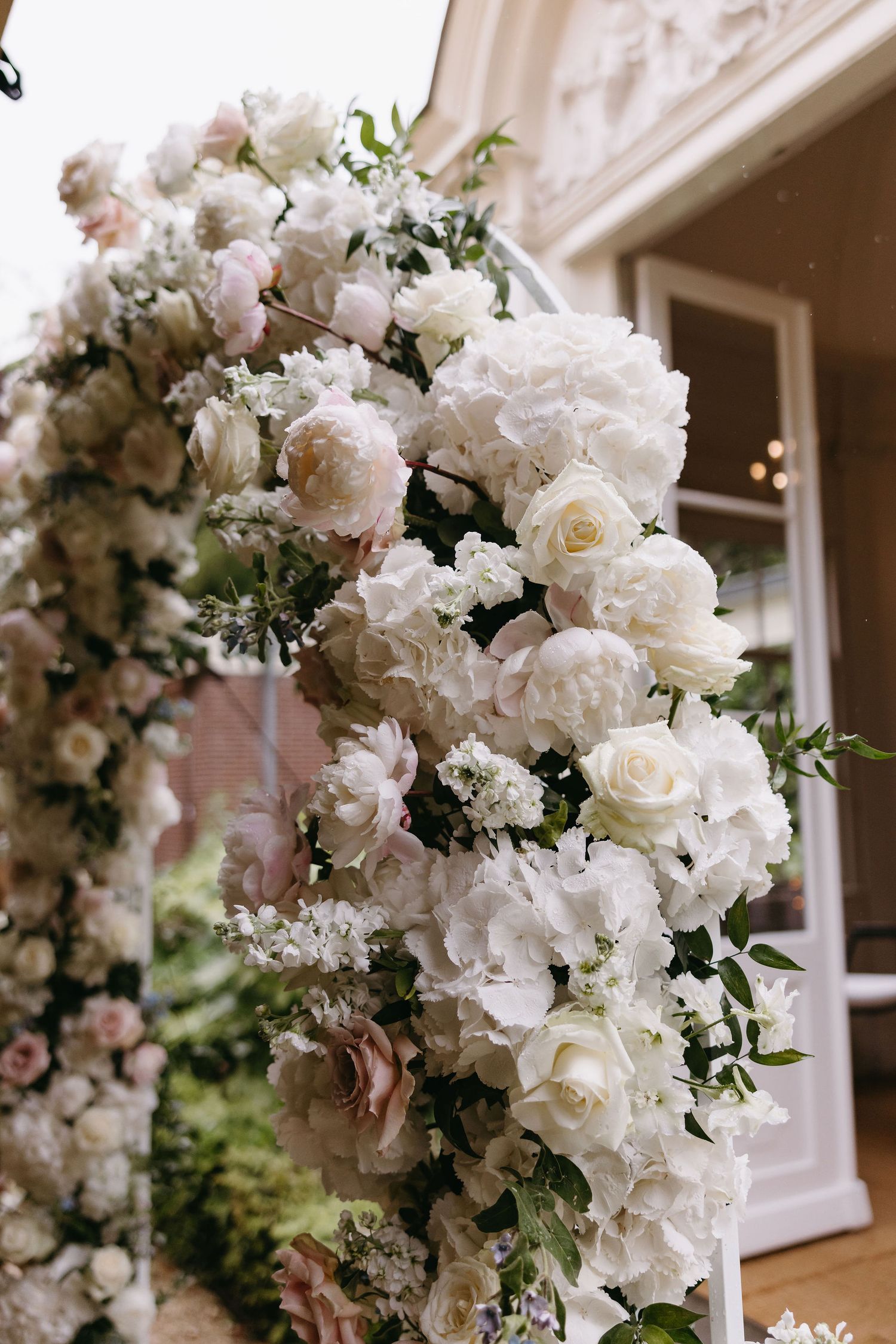 White floral arch with roses and hydrangeas decorated for outdoor wedding ceremony.