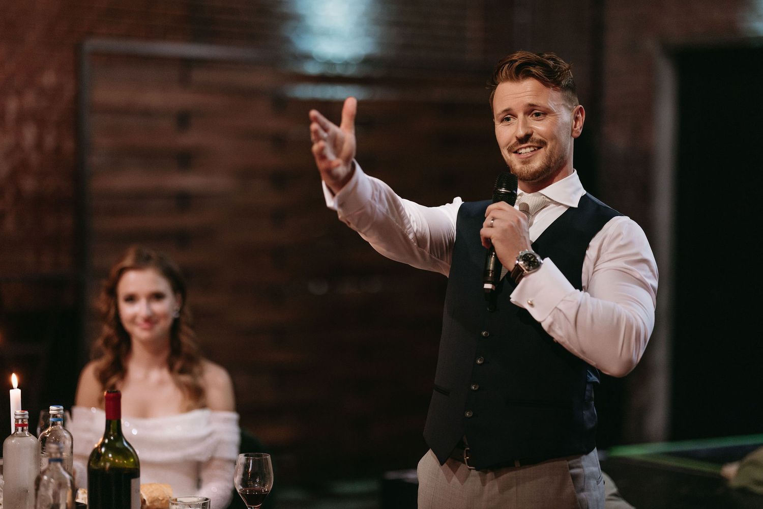 Reception scene with someone making a speech in a vest and white shirt.