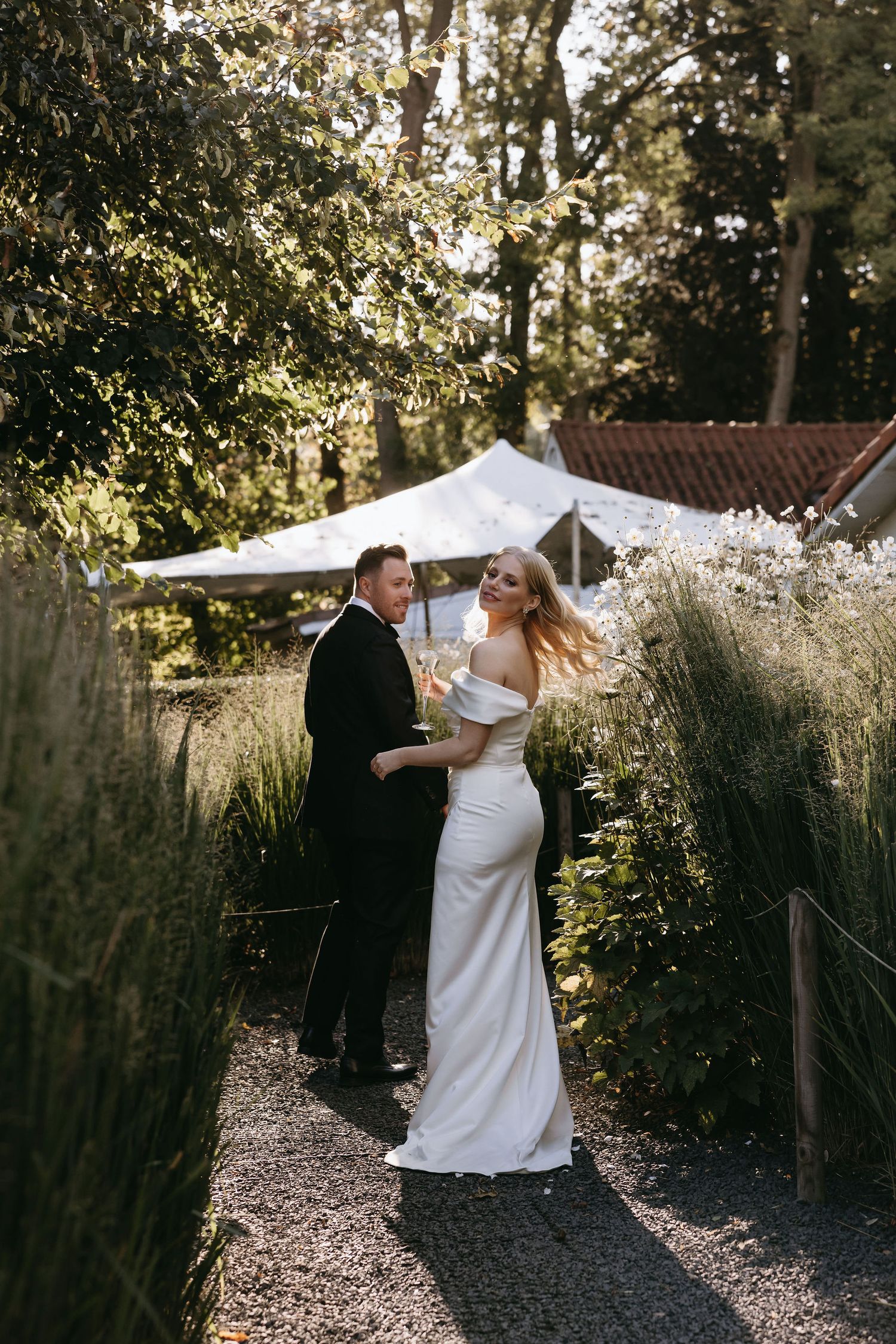 A couple shares an intimate moment on a garden path surrounded by tall grasses and greenery.