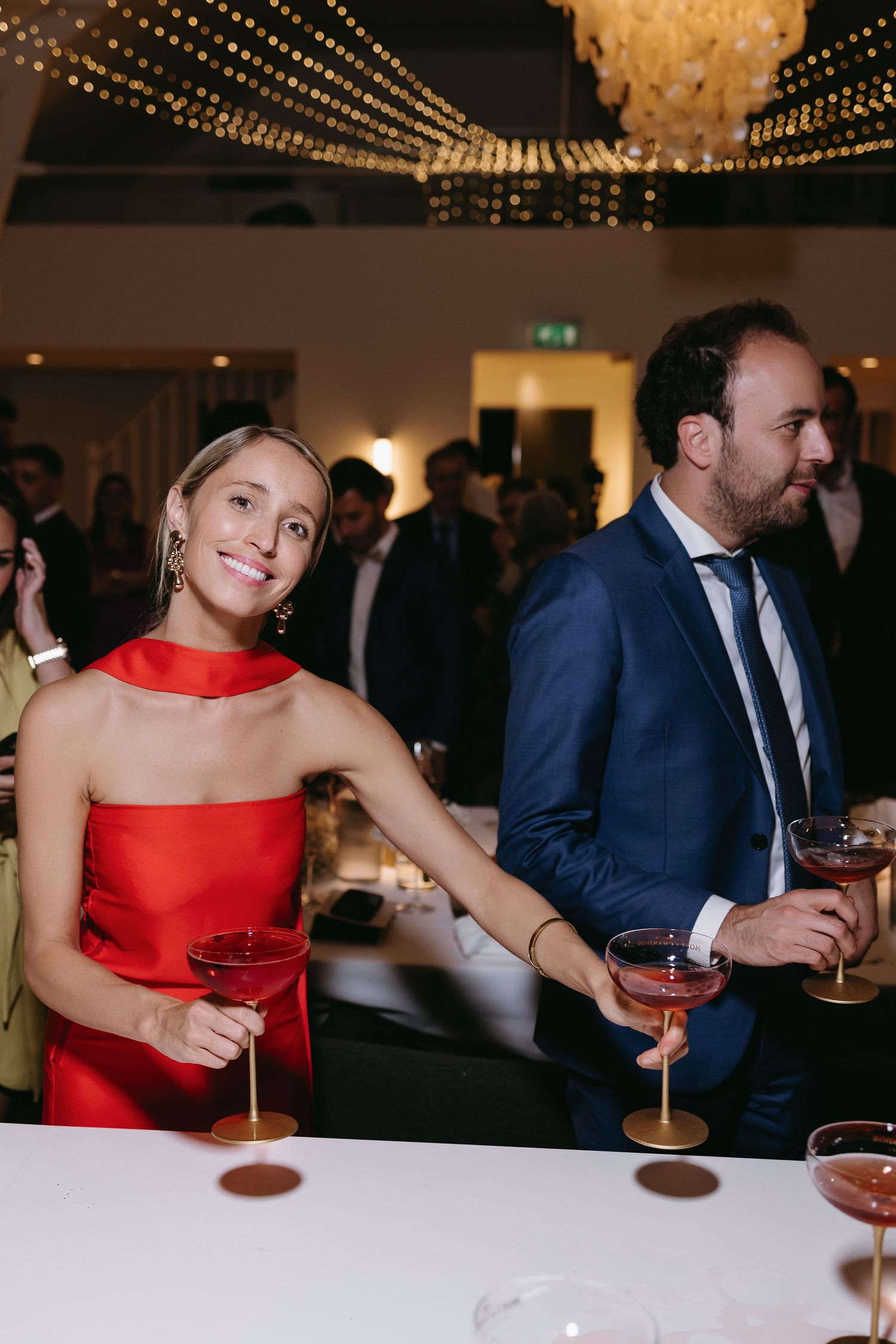 Guests enjoying cocktails at an elegant event under crystal chandeliers.